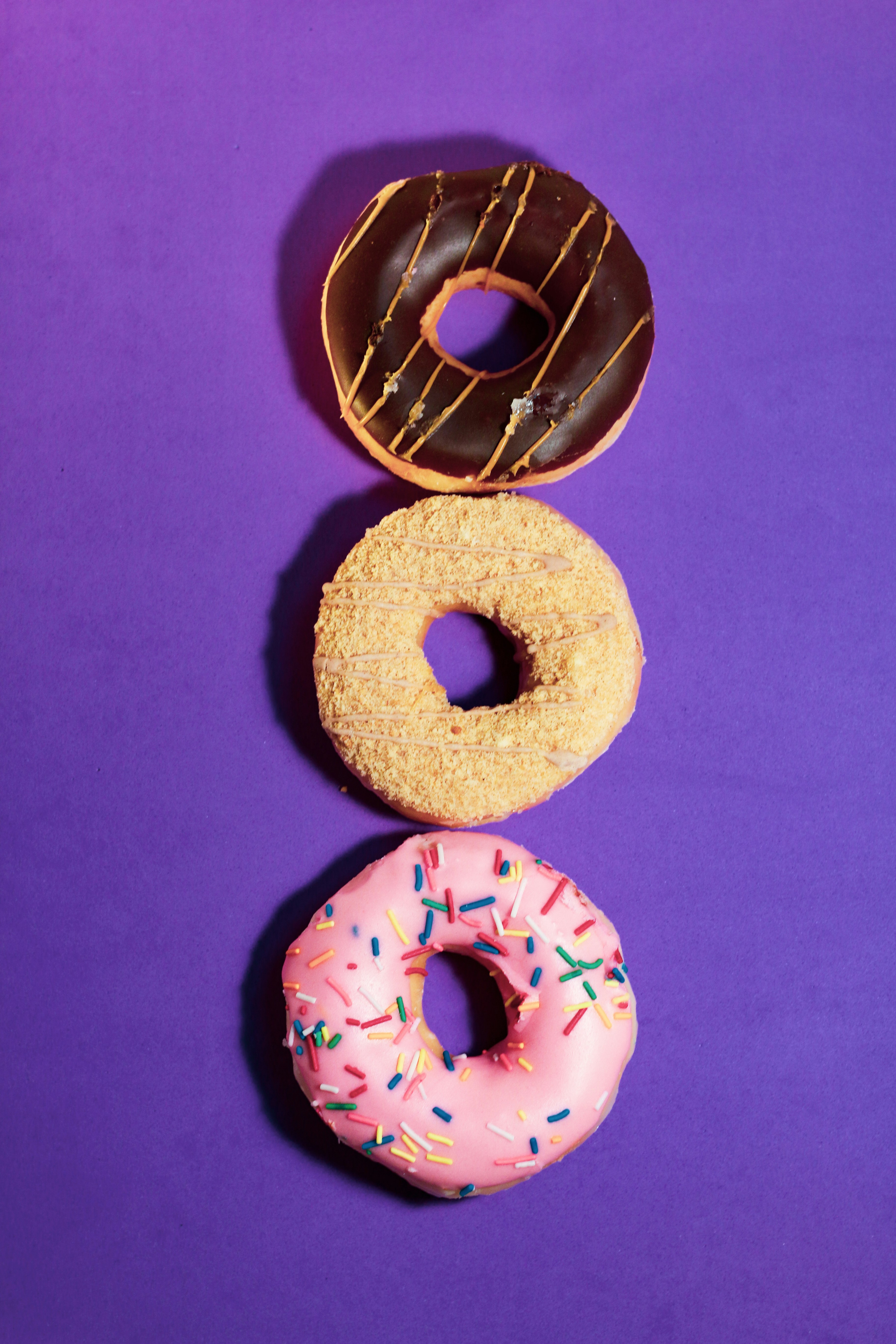 Três donuts com glacê sobre um fundo roxo brilhante.