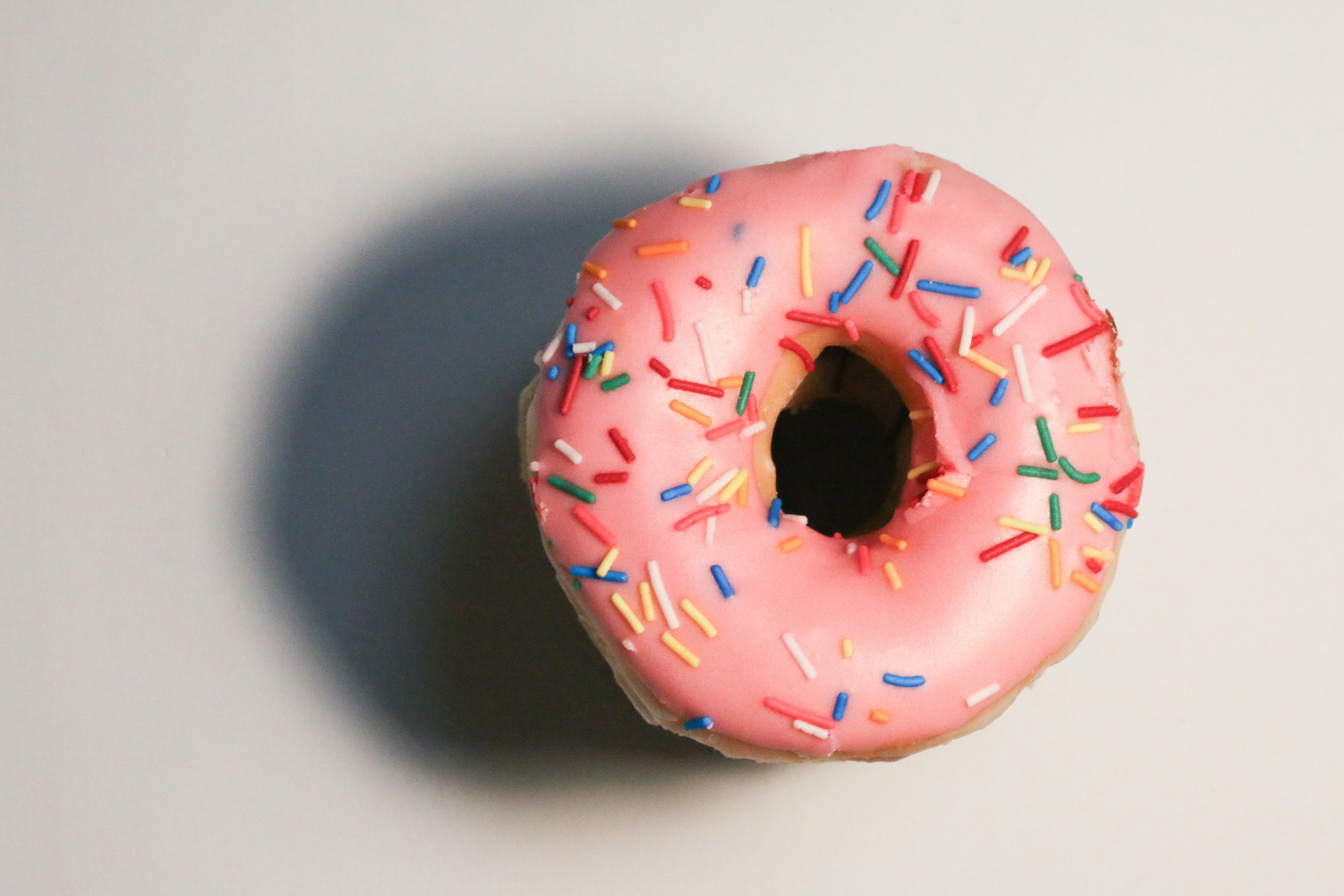 Um donut rosa com granulados coloridos sobre um fundo branco.