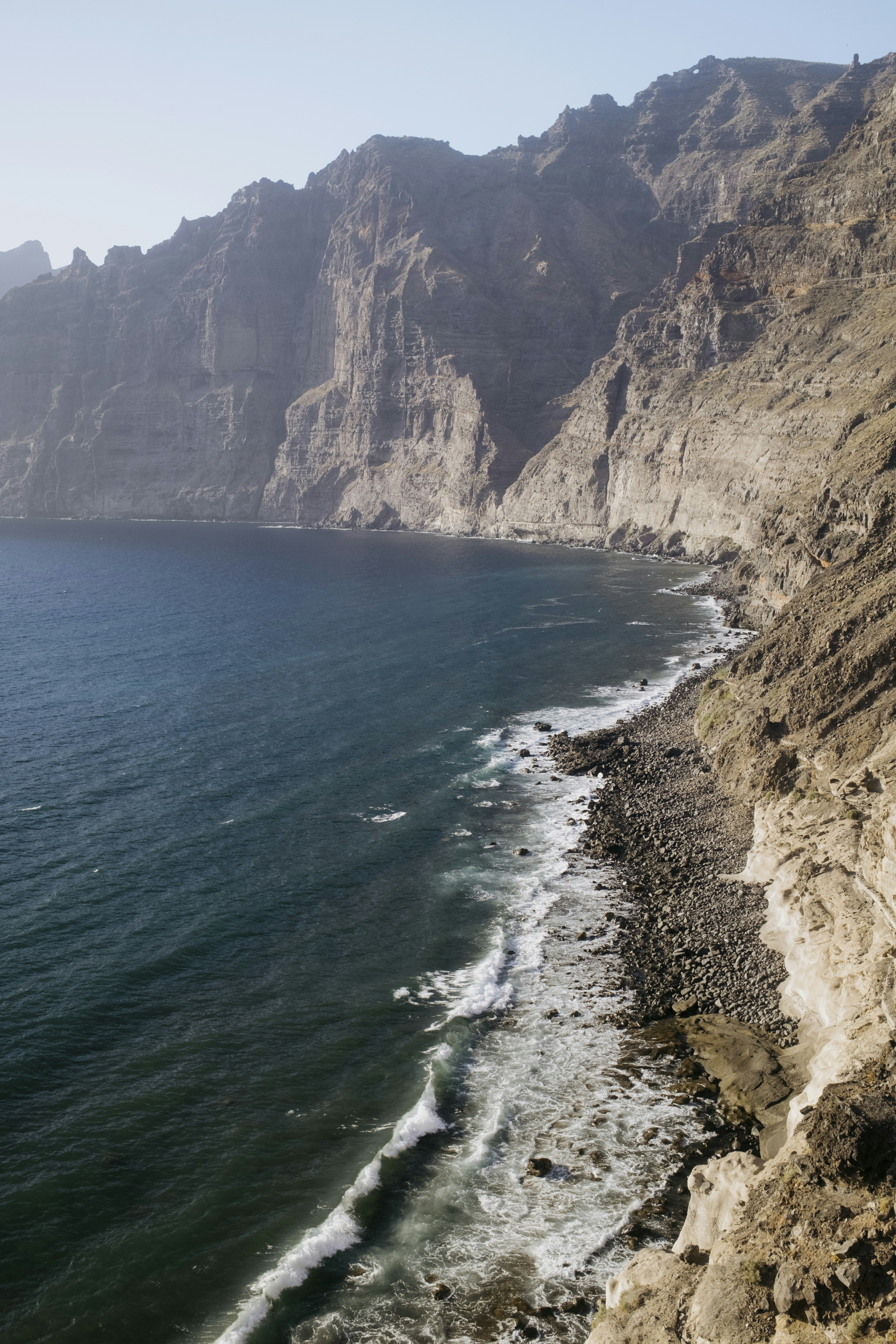 Towering cliffs overlook a rocky beach and deep blue ocean.