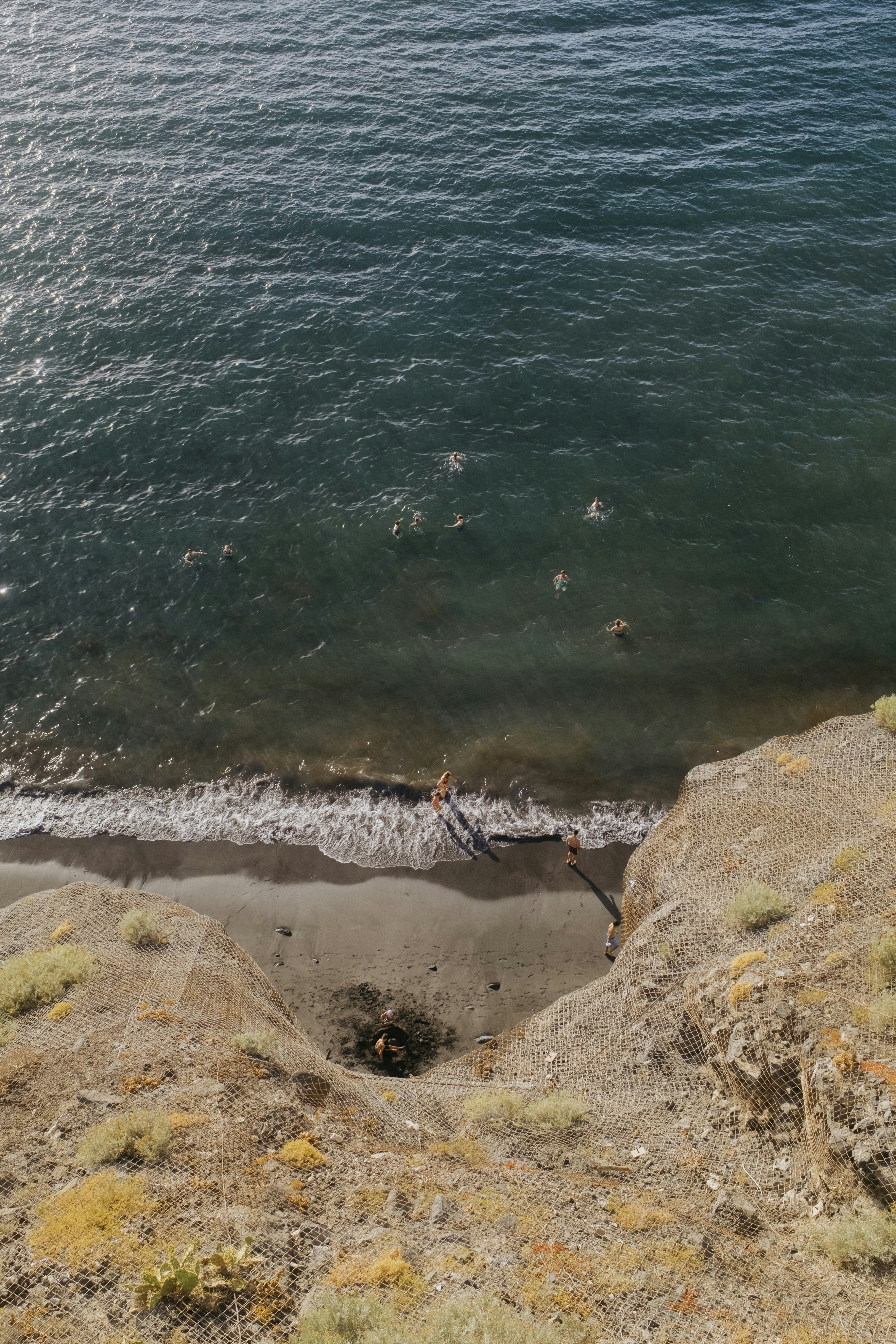 People swimming and standing on a small beach from above.