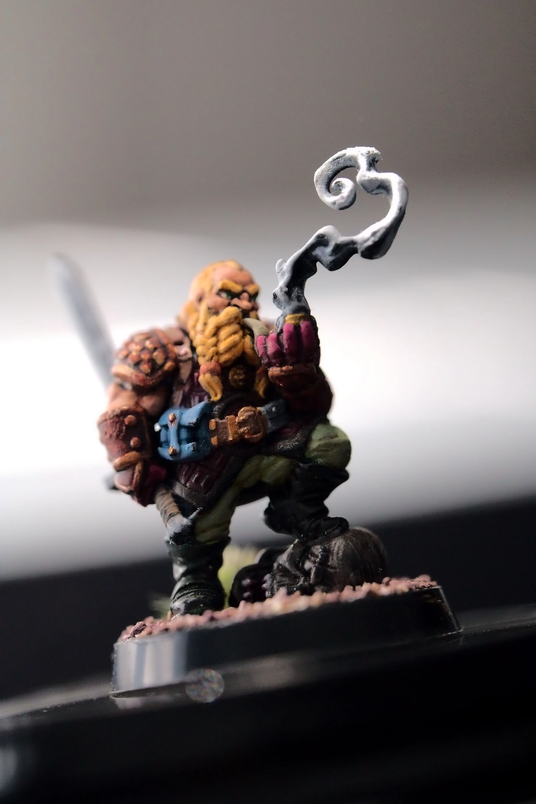 Close-up of a painted dwarf figure with an orange beard and a red coat on a textured round base