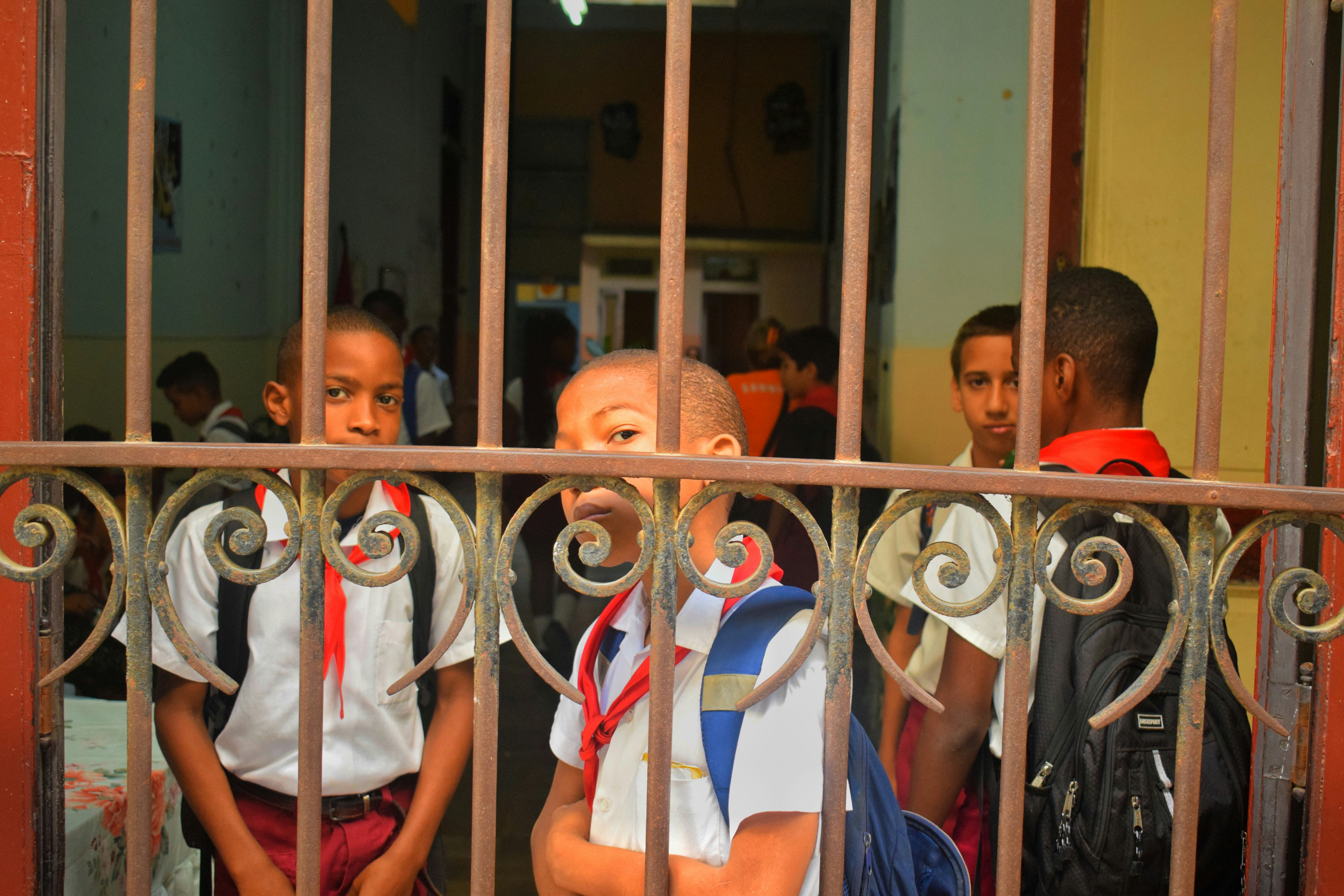 A group of parents and media persons gathered outside a school gate, some holding signs or talking animatedly, depicting a protest or media scrum.