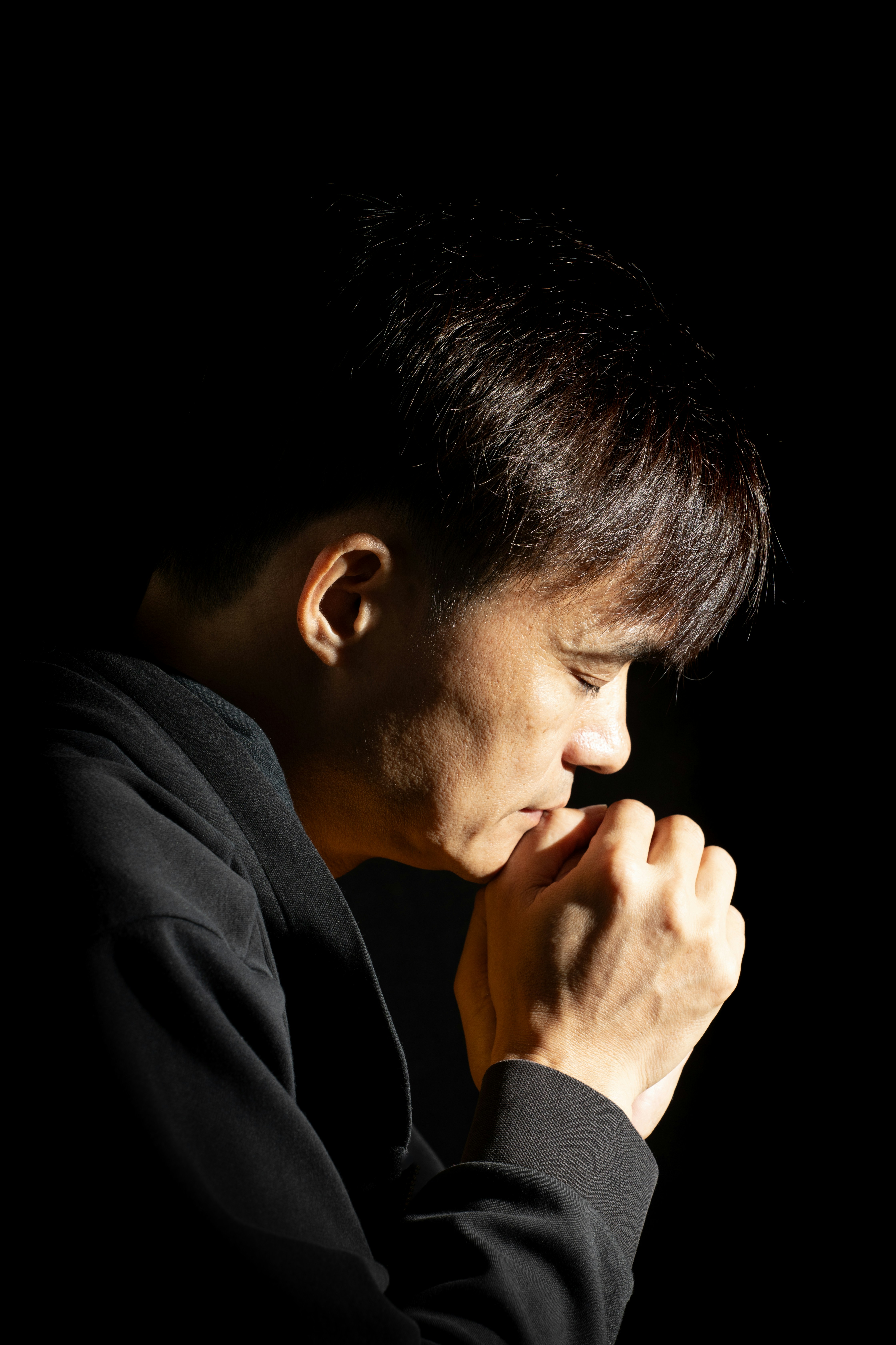 Man praying with clasped hands against a dark background