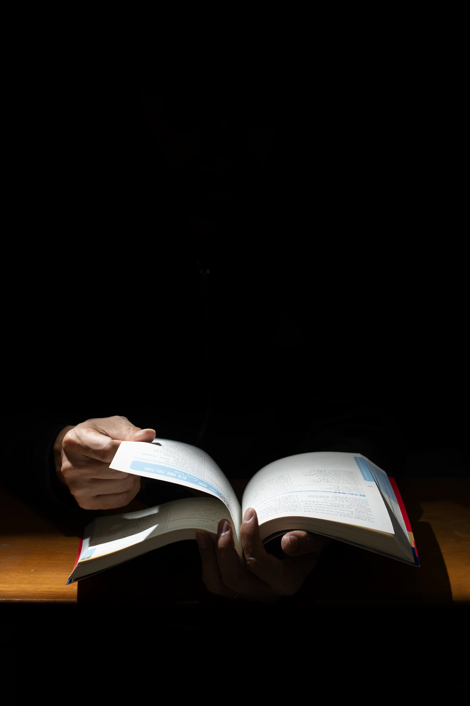 Hands turning the pages of a large open register in a dark room