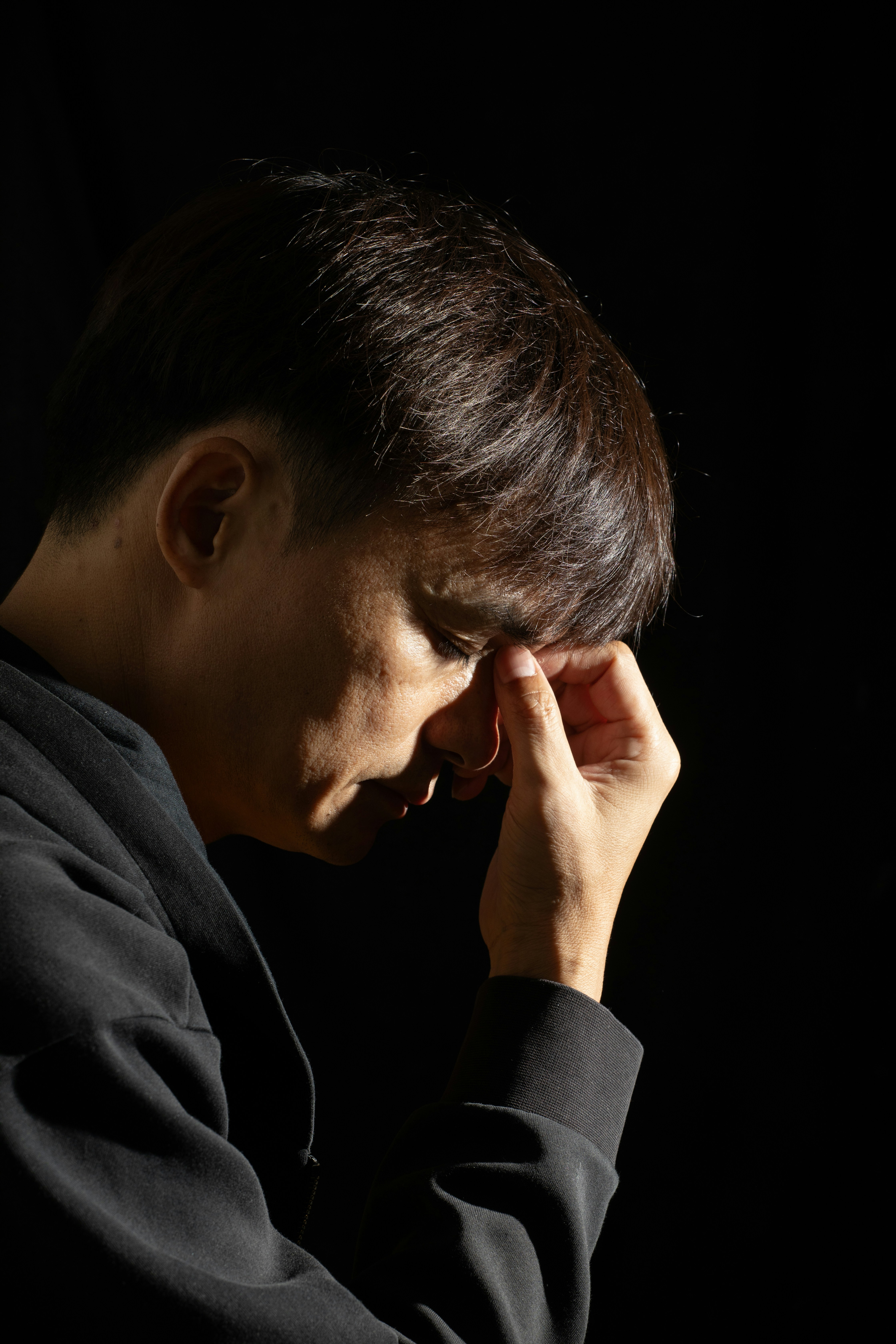 A man in dark clothes holds his forehead in thought.