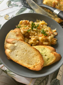 A bowl of cheesy scrambled eggs with toasted garlic bread.