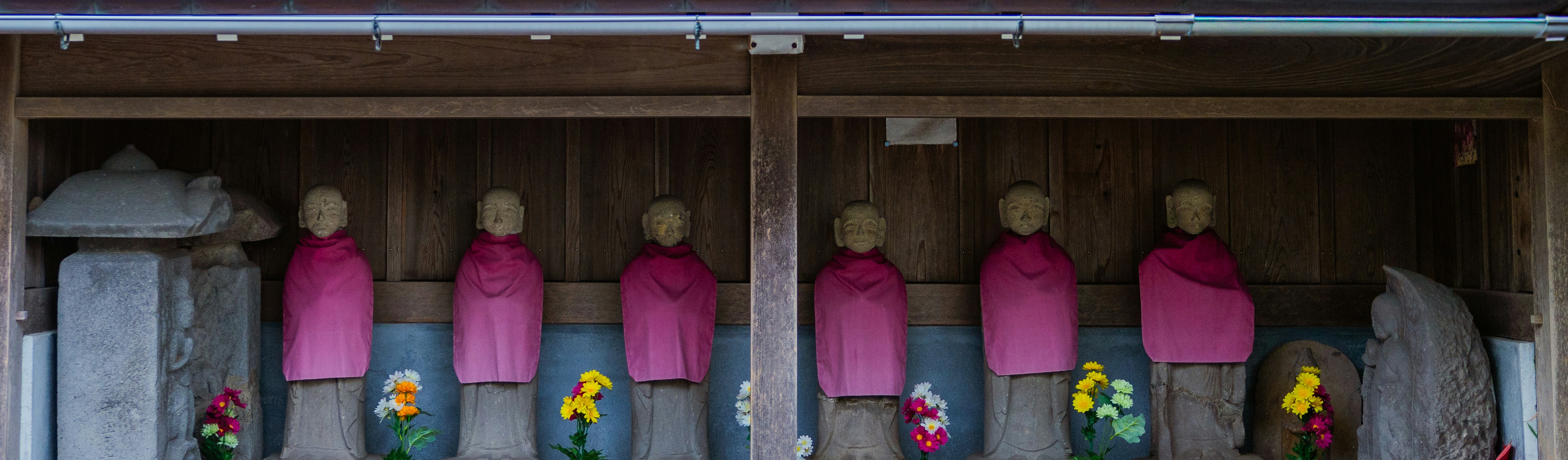 Multiple jizo statues in pink robes with flowers.