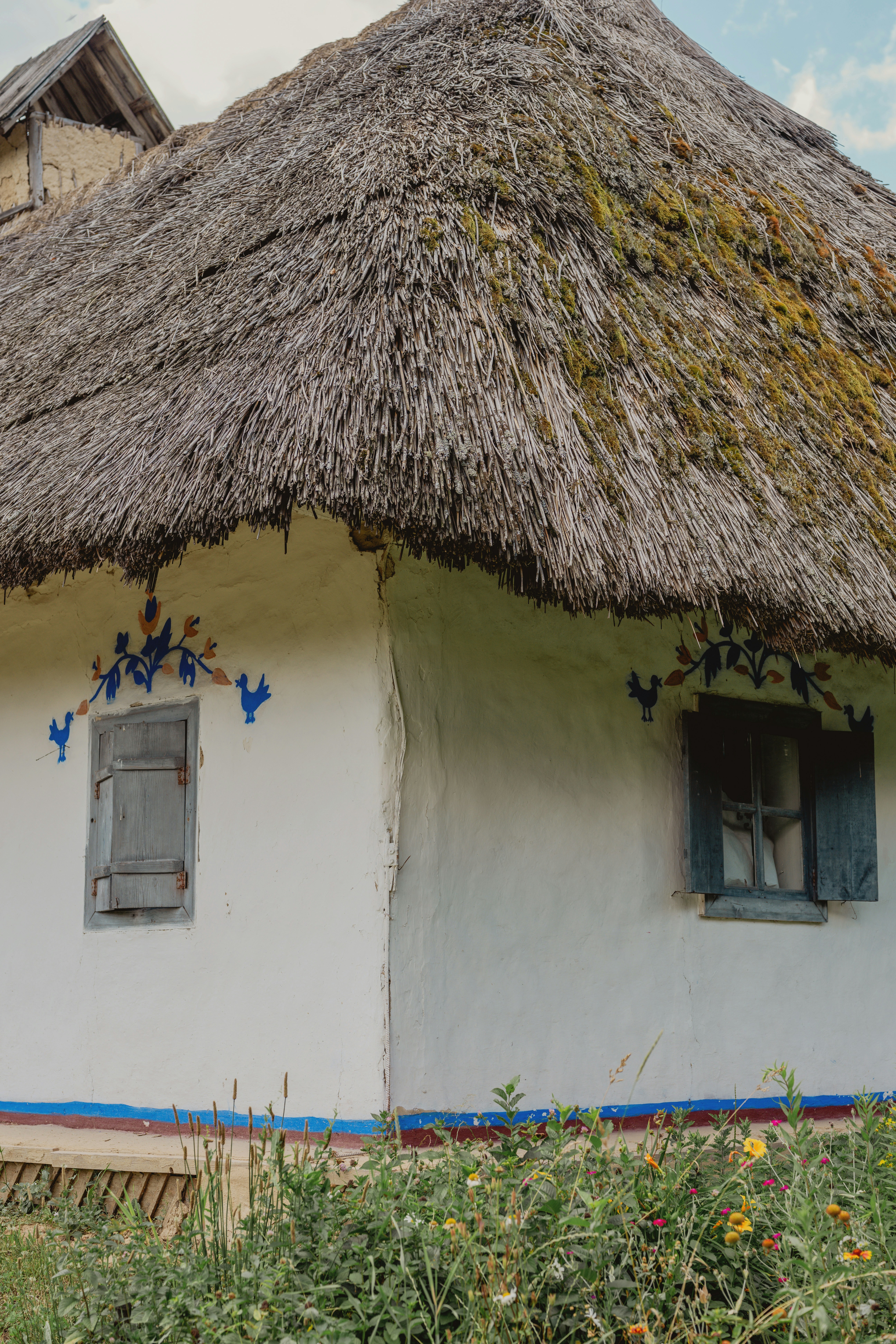 Casa branca tradicional com telhado de palha e pássaros pintados de azul.