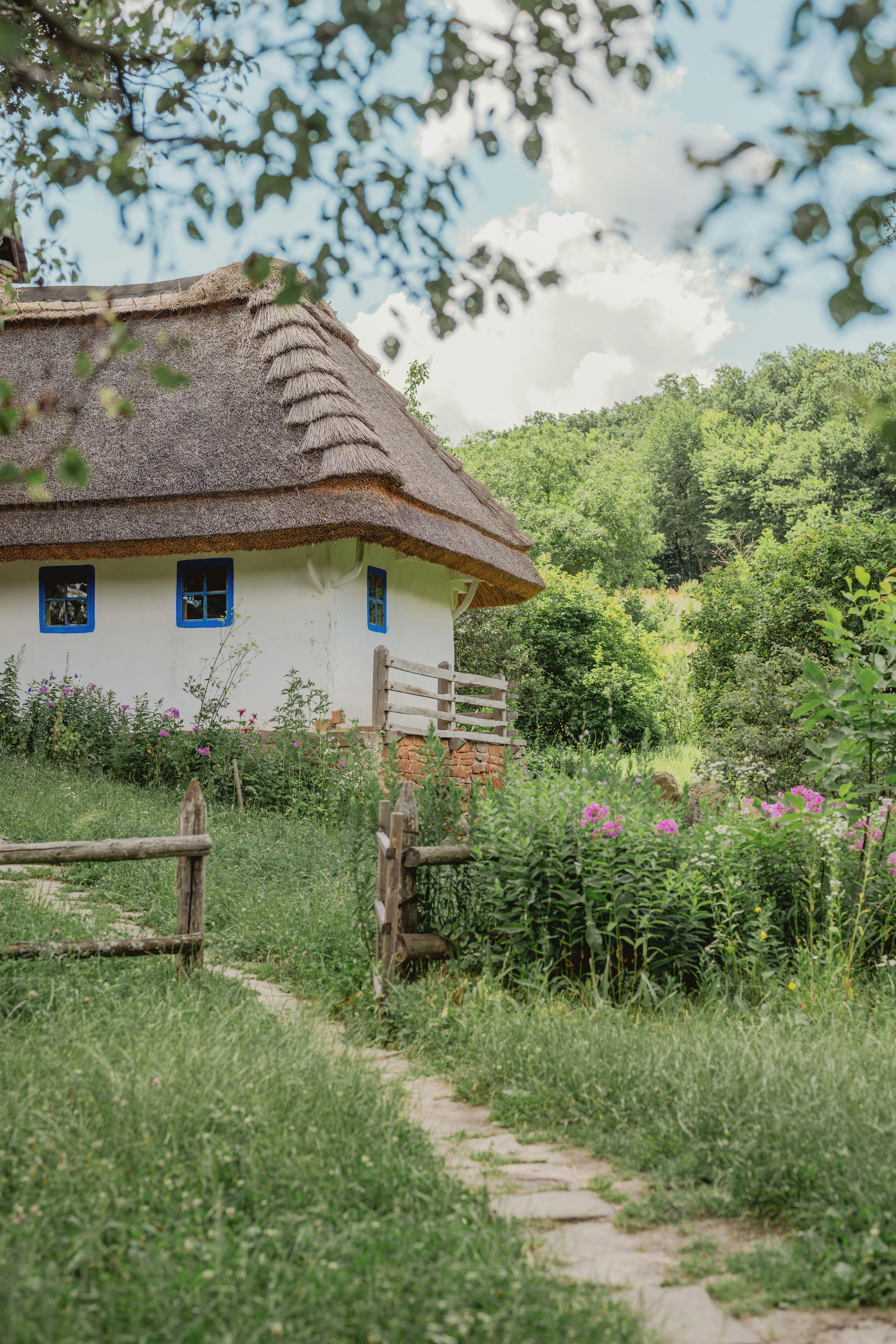Casa rústica com telhado de palha e janelas azuis na natureza.