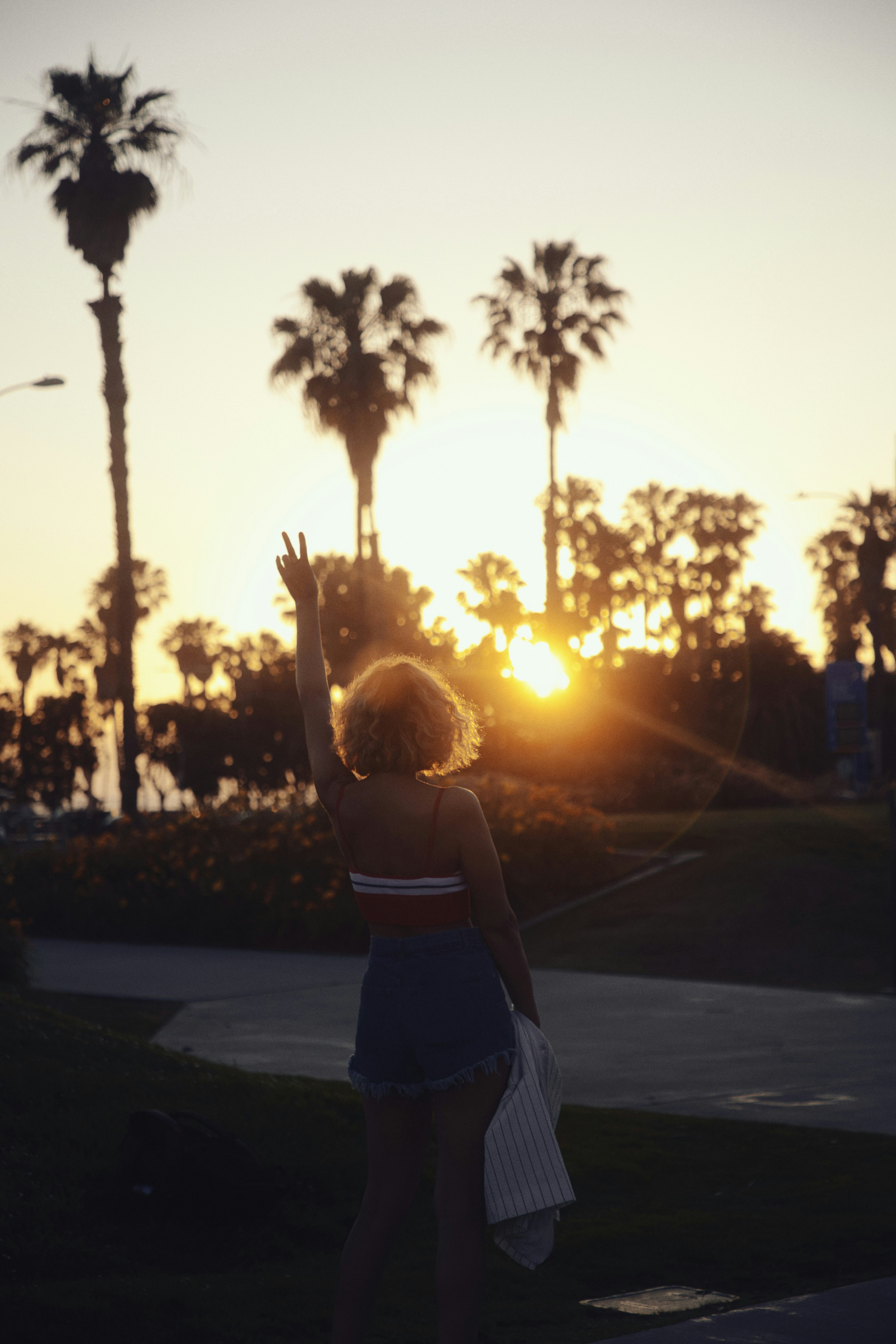 Femme faisant le signe de paix, palmiers au coucher du soleil