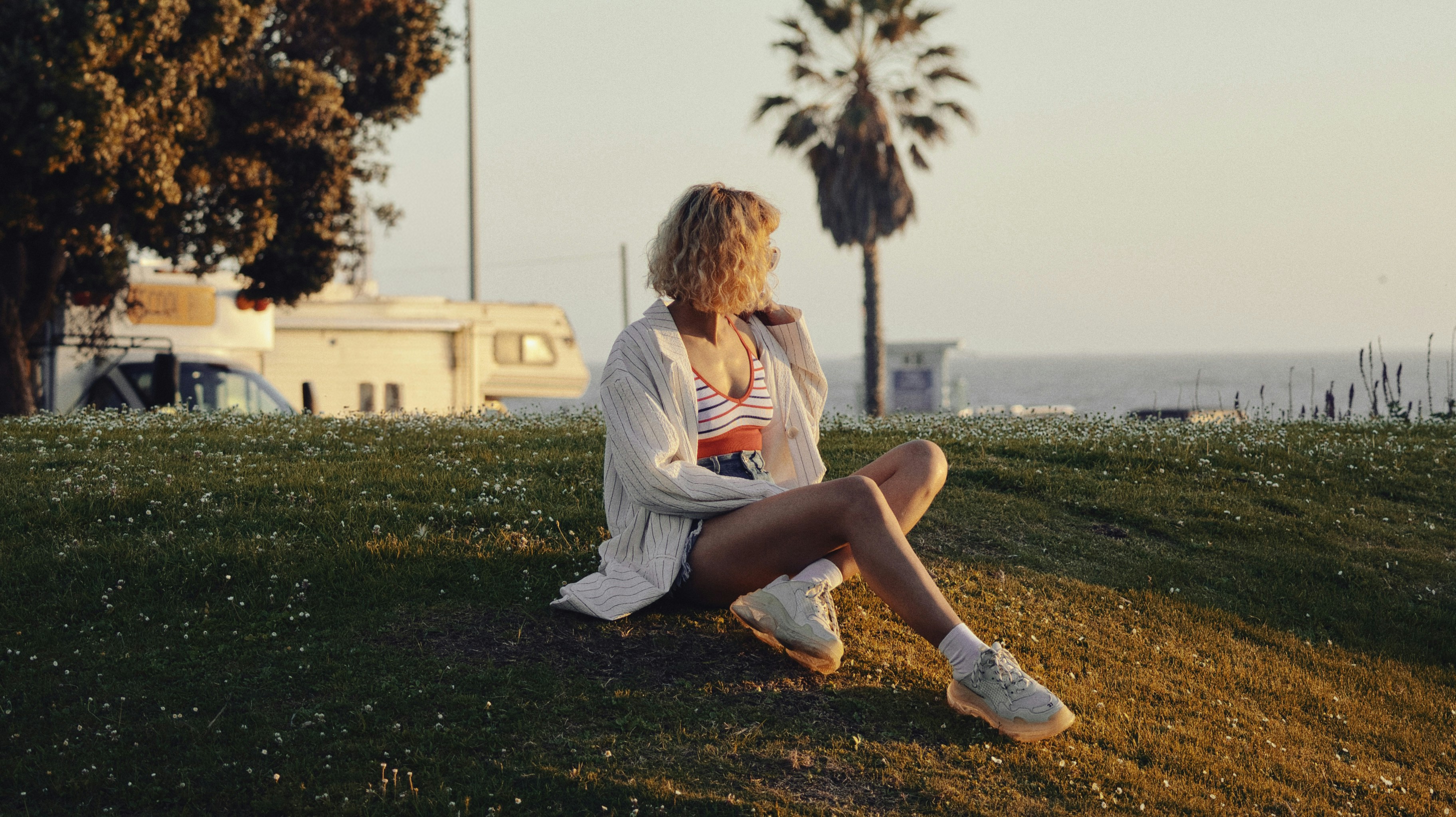 Woman sits on grassy hill near ocean at sunset