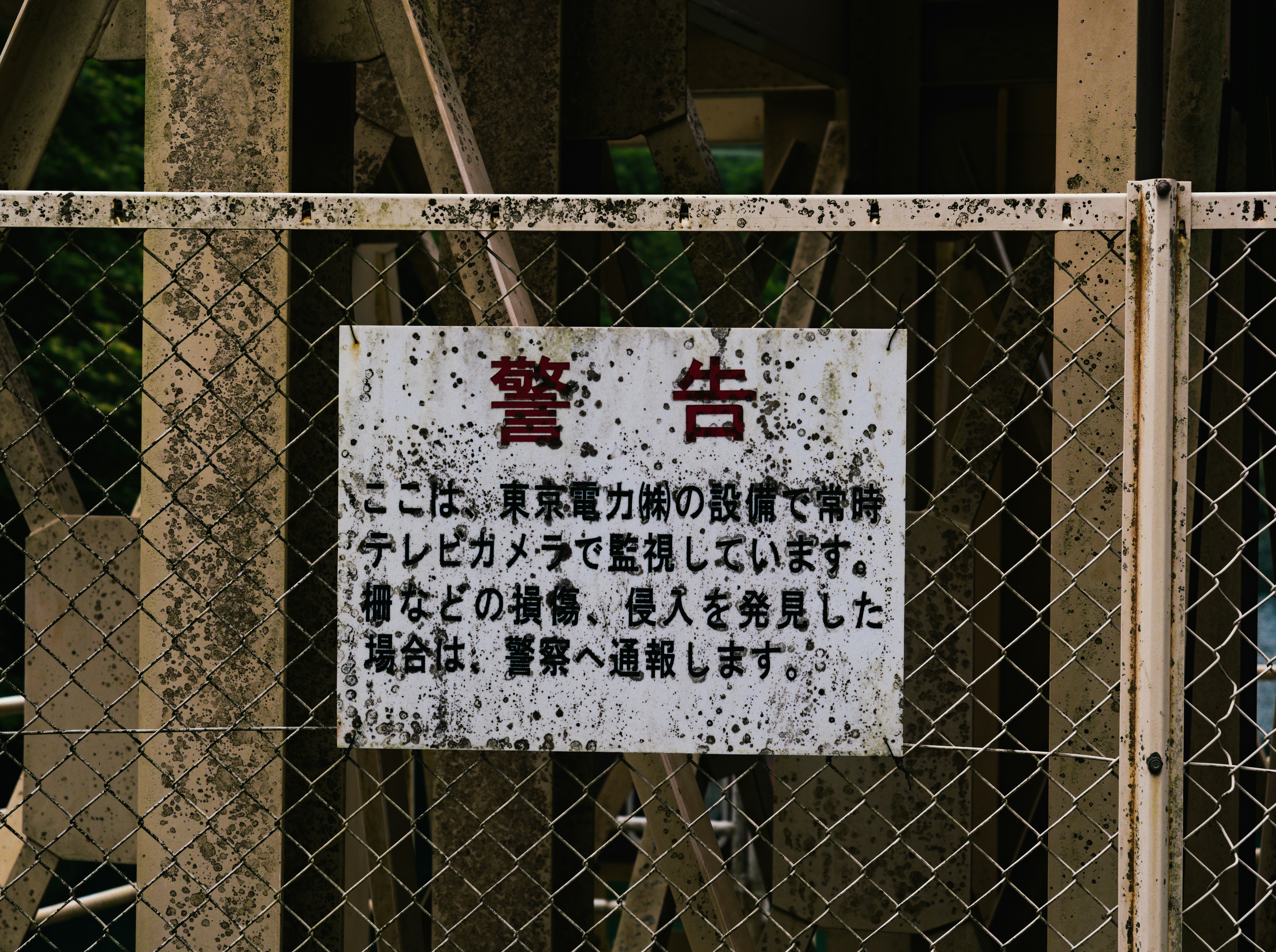 Weathered japanese warning sign on a chain-link fence