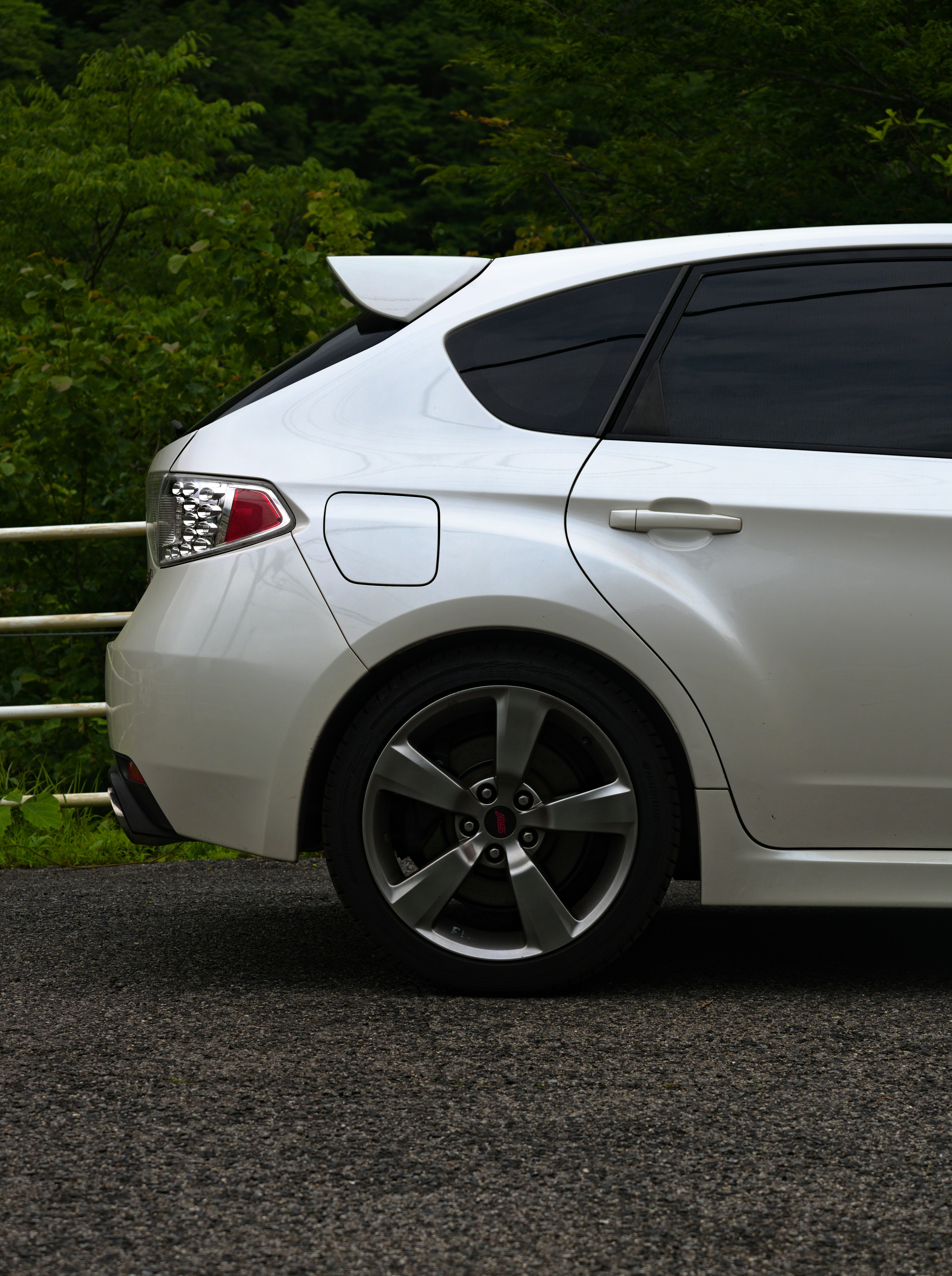 White hatchback car parked with green trees in background