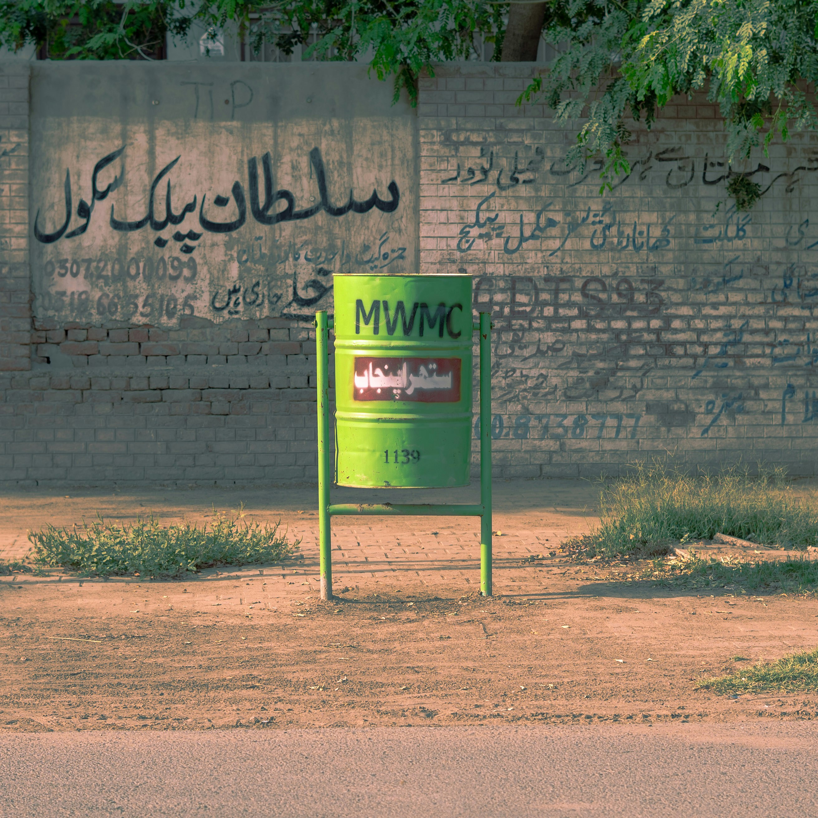 Green trash bin against a graffiti-covered wall.