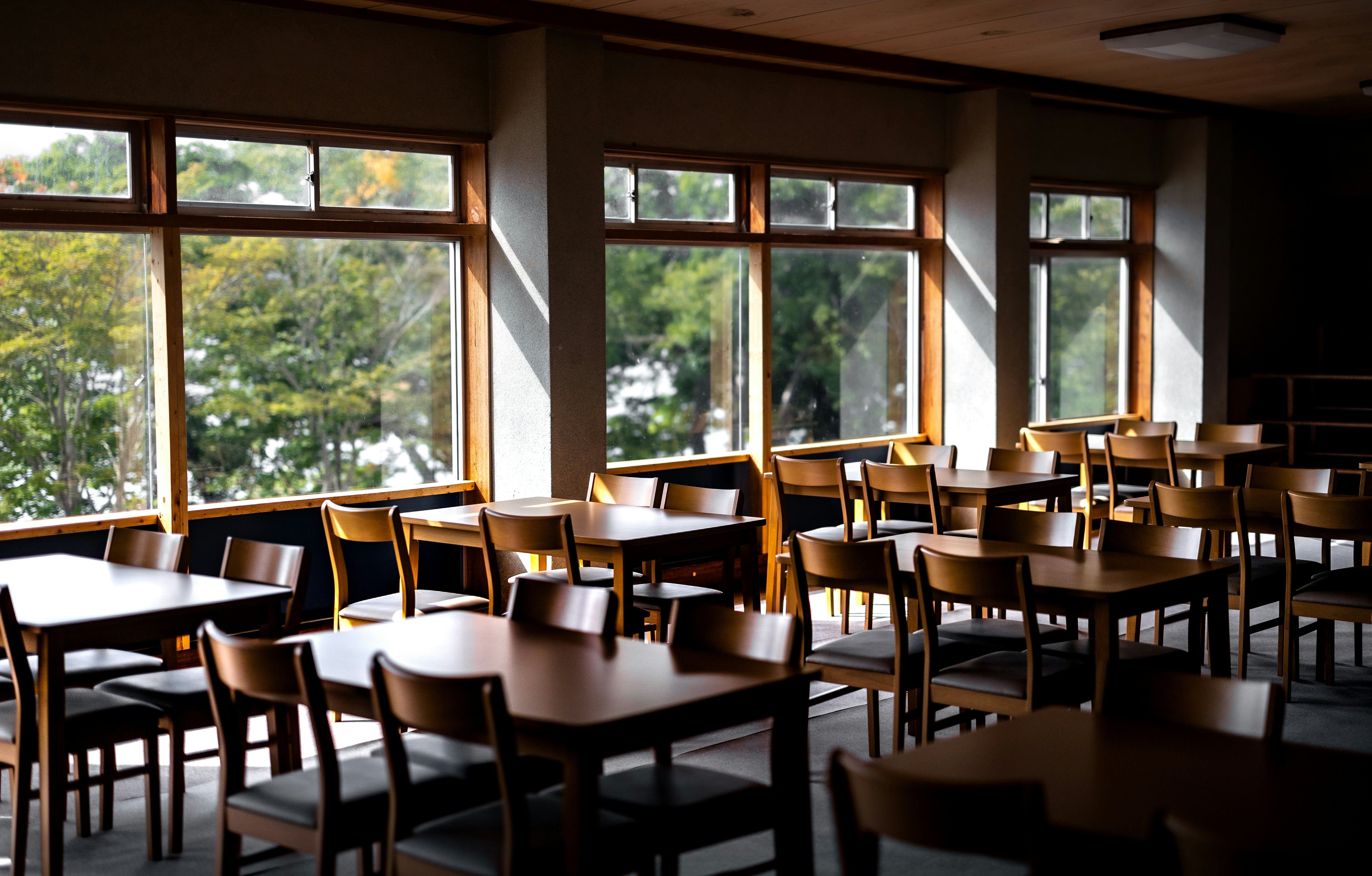 An empty dining hall with tables, chairs, and large windows.