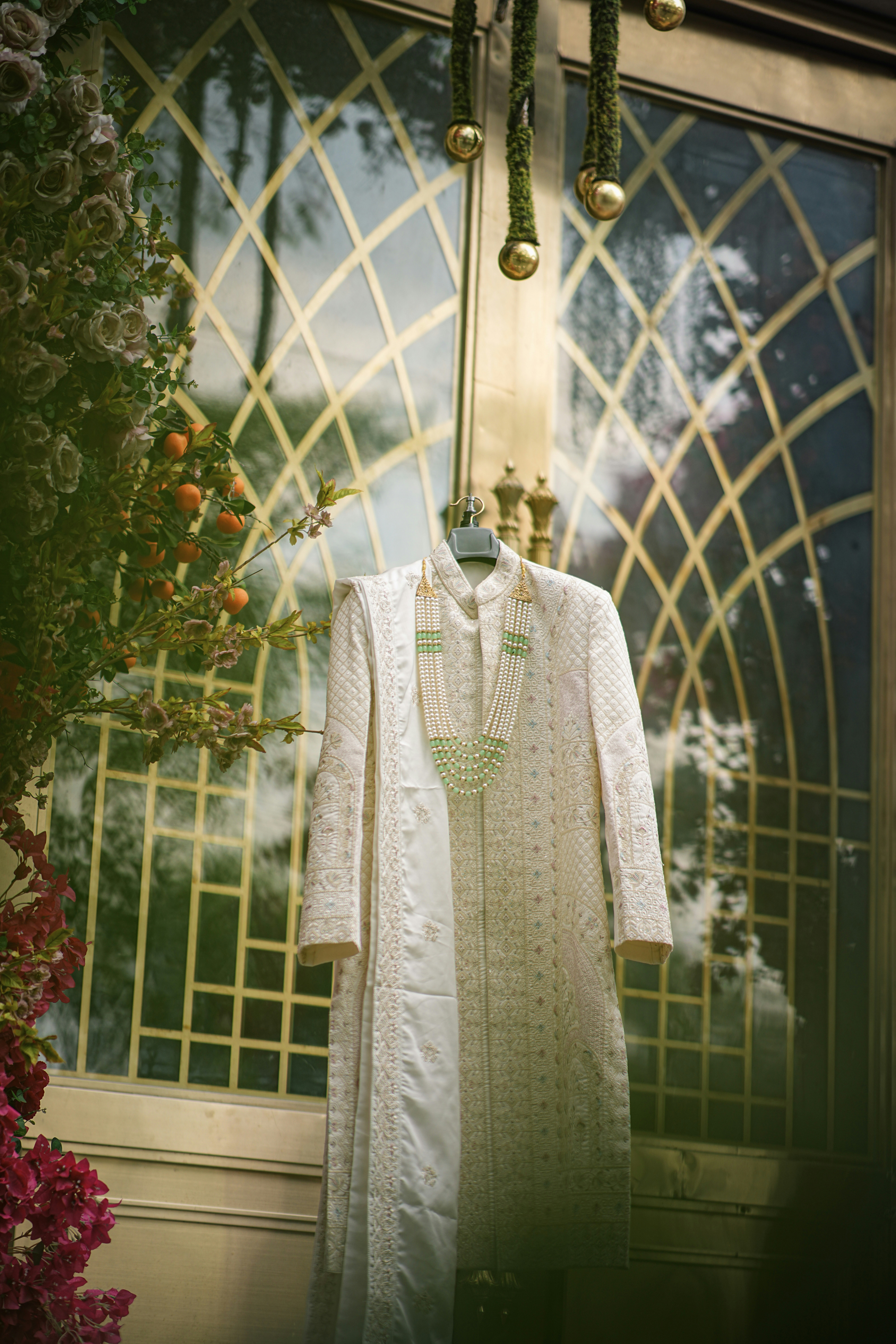 A white sherwani and necklace hanging on a golden door.