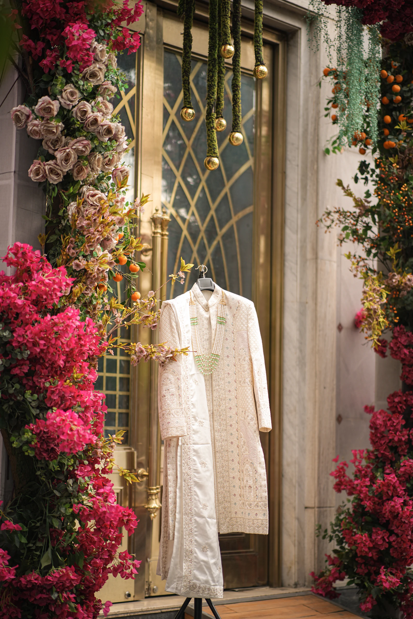 Cream embroidered sherwani hanging in front of a decorated golden door