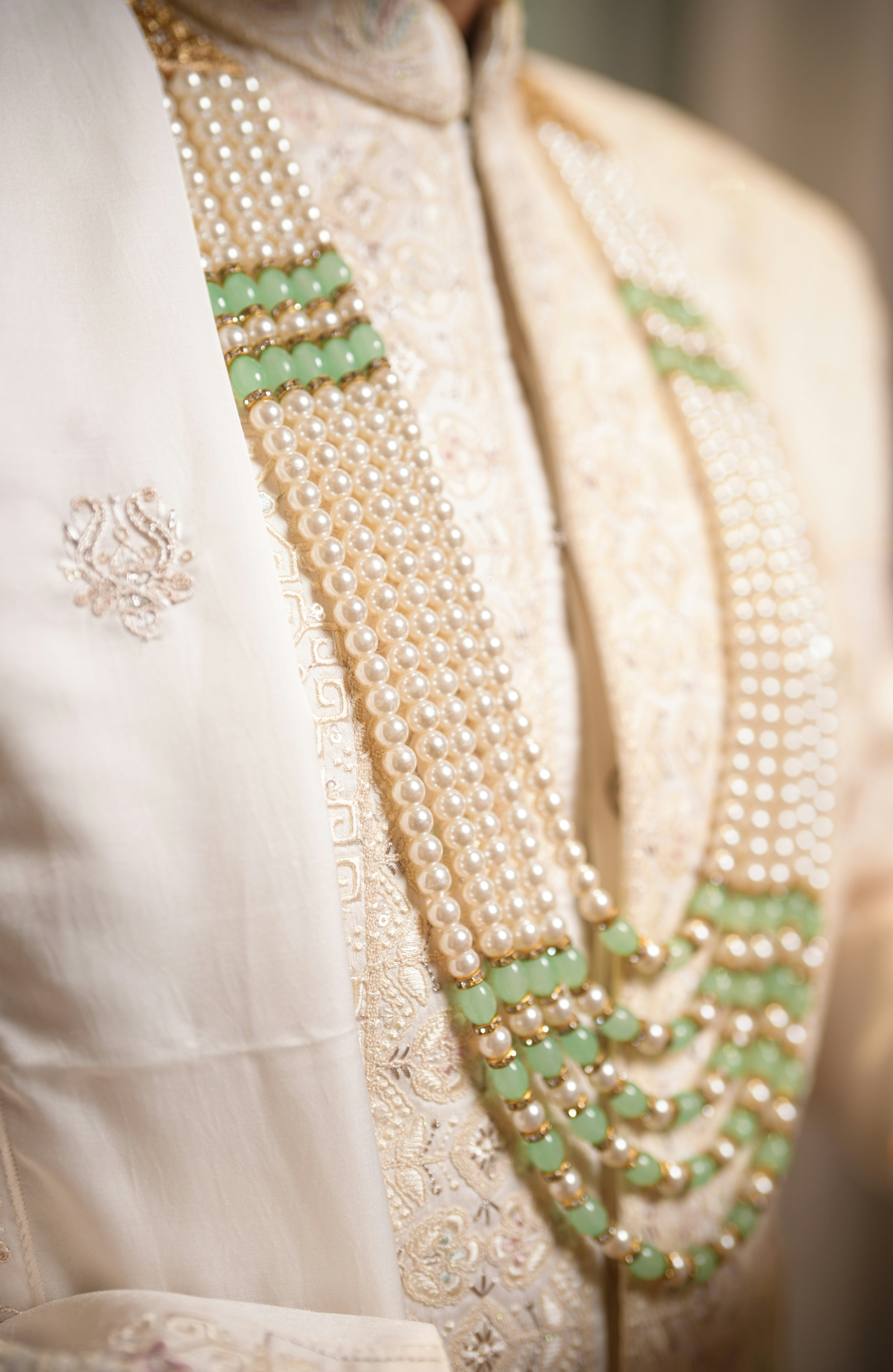A groom wears a traditional pearl and green bead necklace.