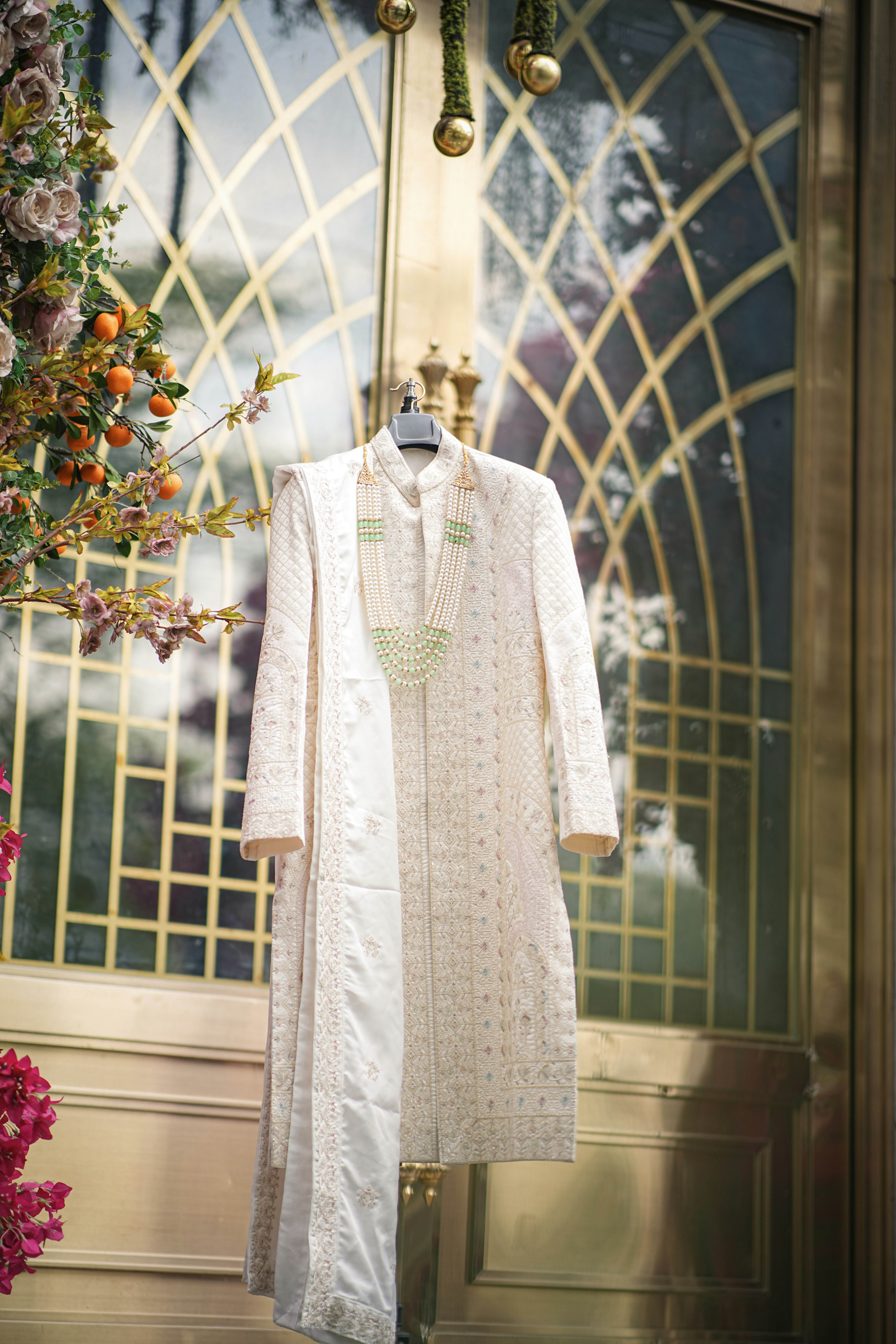 White embroidered indian sherwani with green necklace.