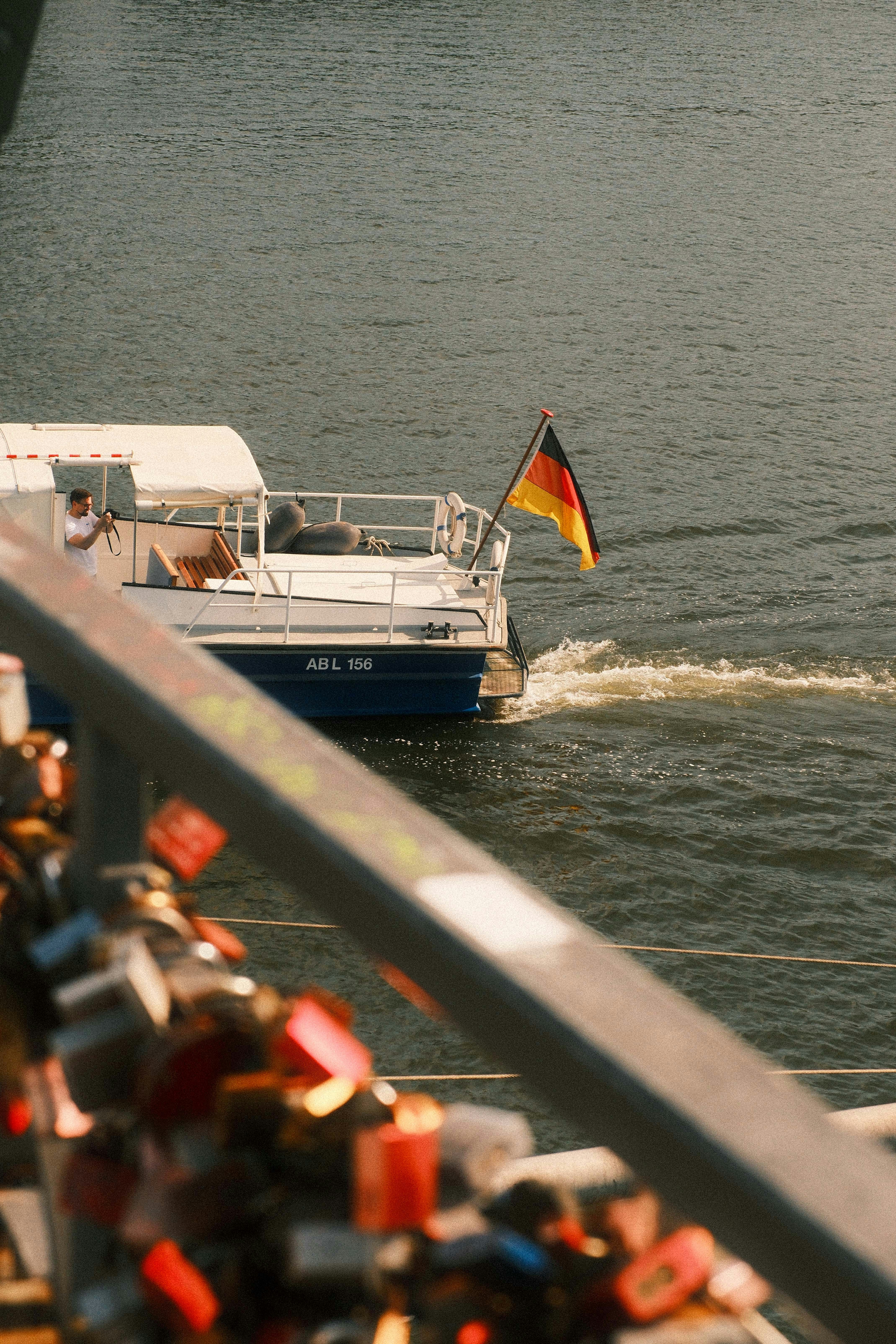 Boat with german flag on river, padlocks on bridge railing.