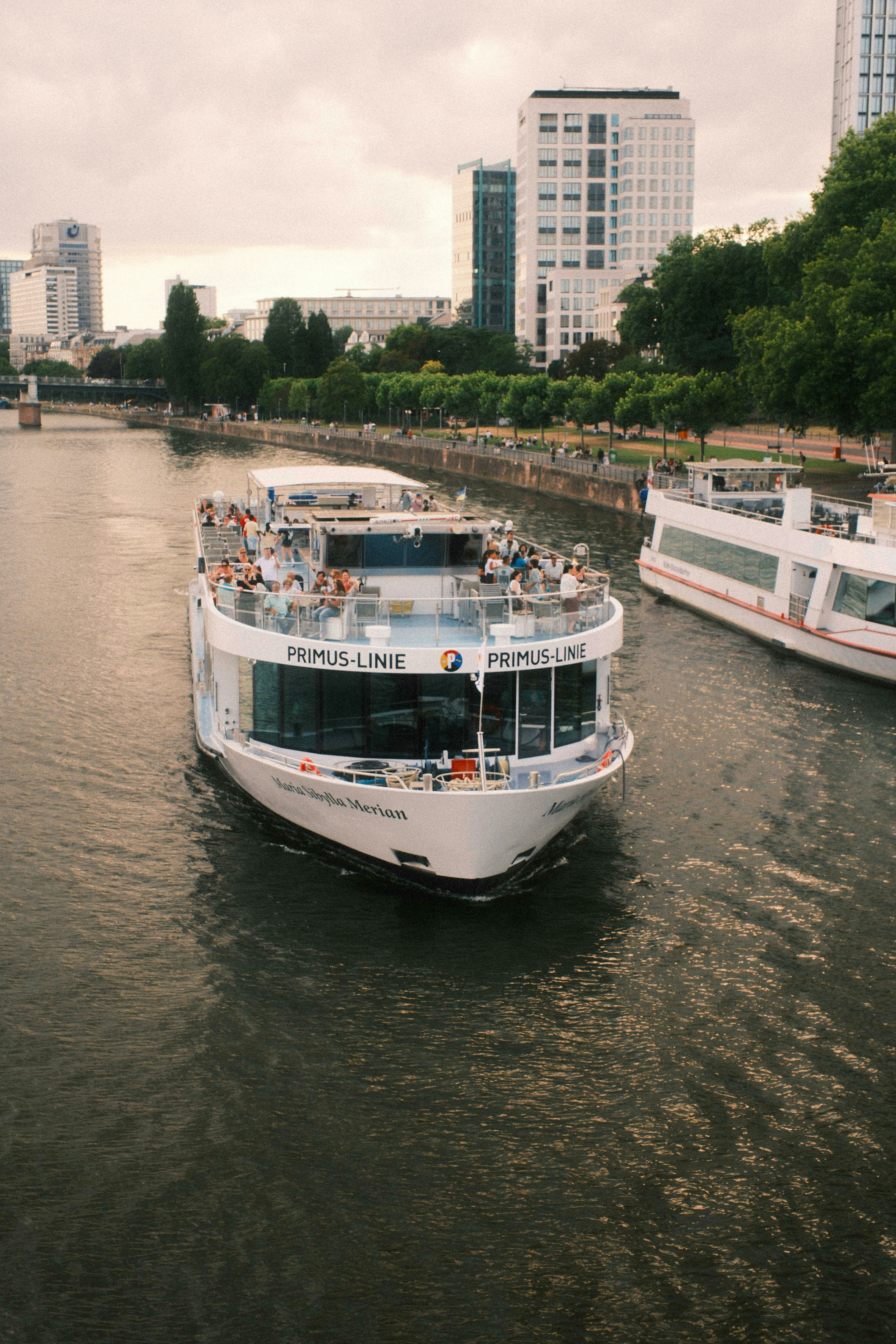 A white passenger boat on a river with city buildings