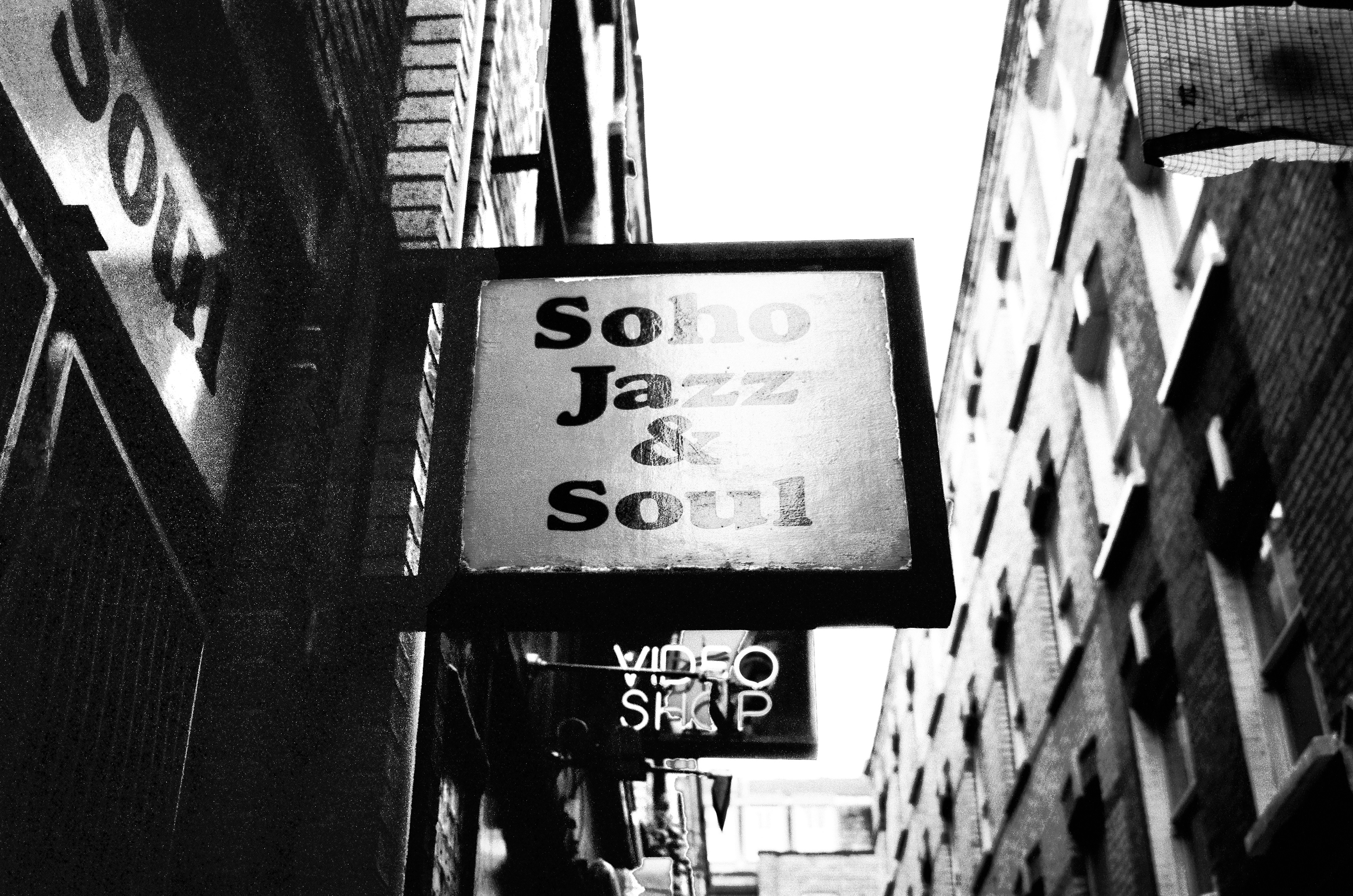 A cinematic, high-contrast black and white film photograph capturing the iconic street signage of \