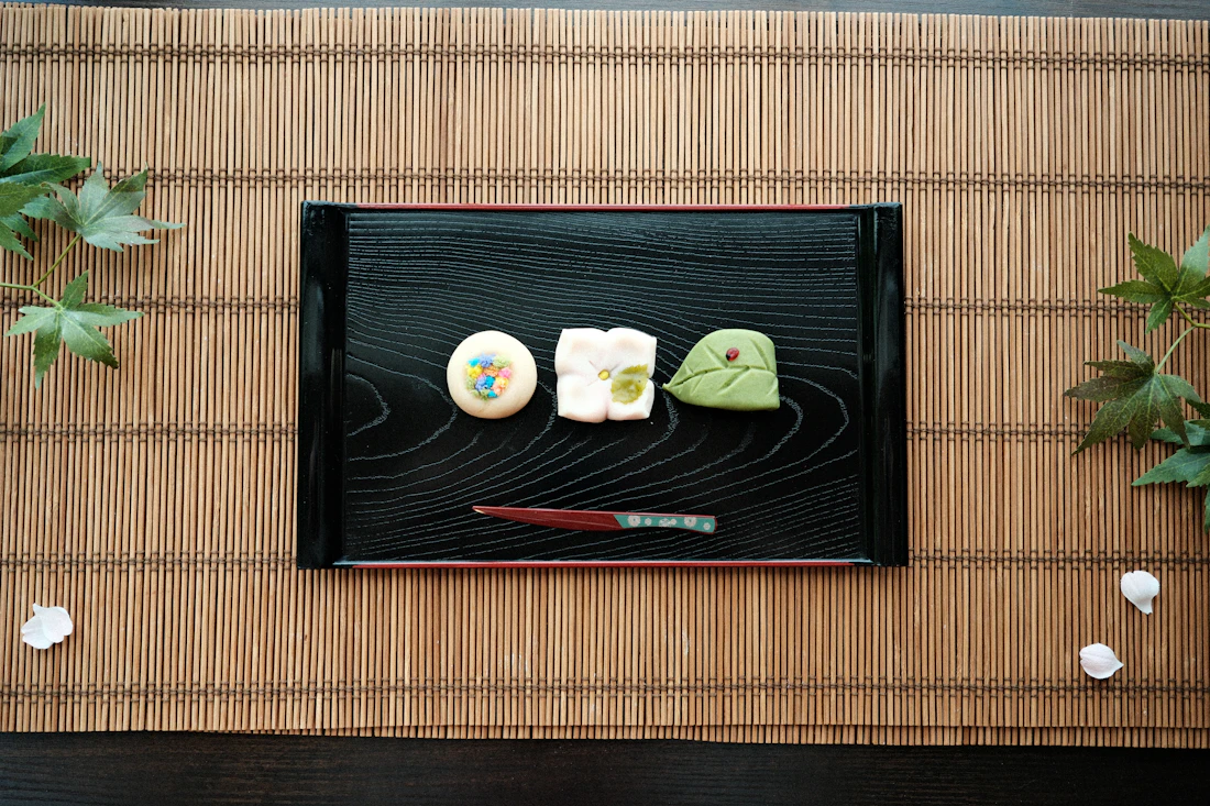 Three small Japanese sweets and a wooden pick on a black lacquer tray