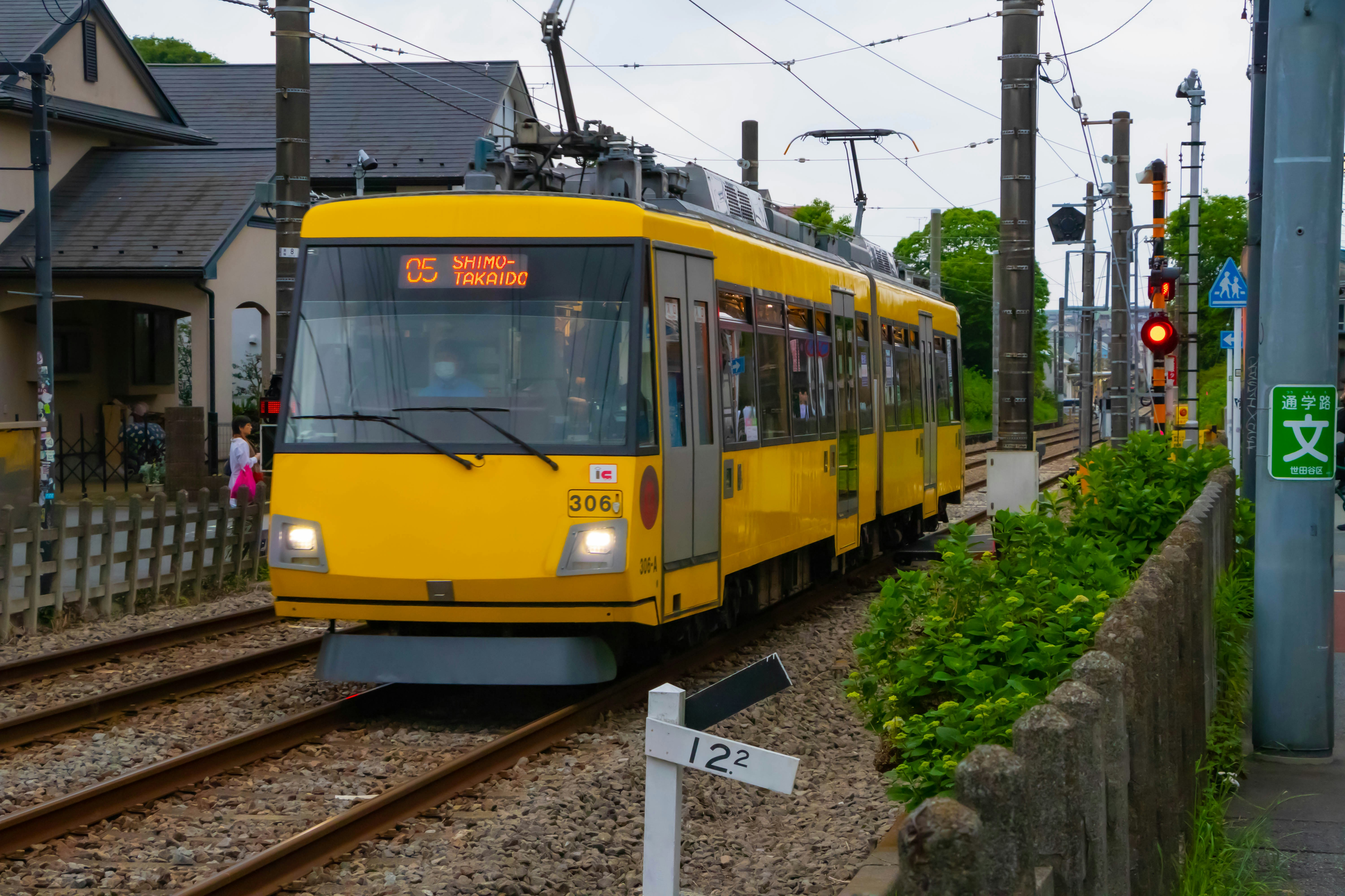 Yellow tram travels on tracks past buildings and green bushes.