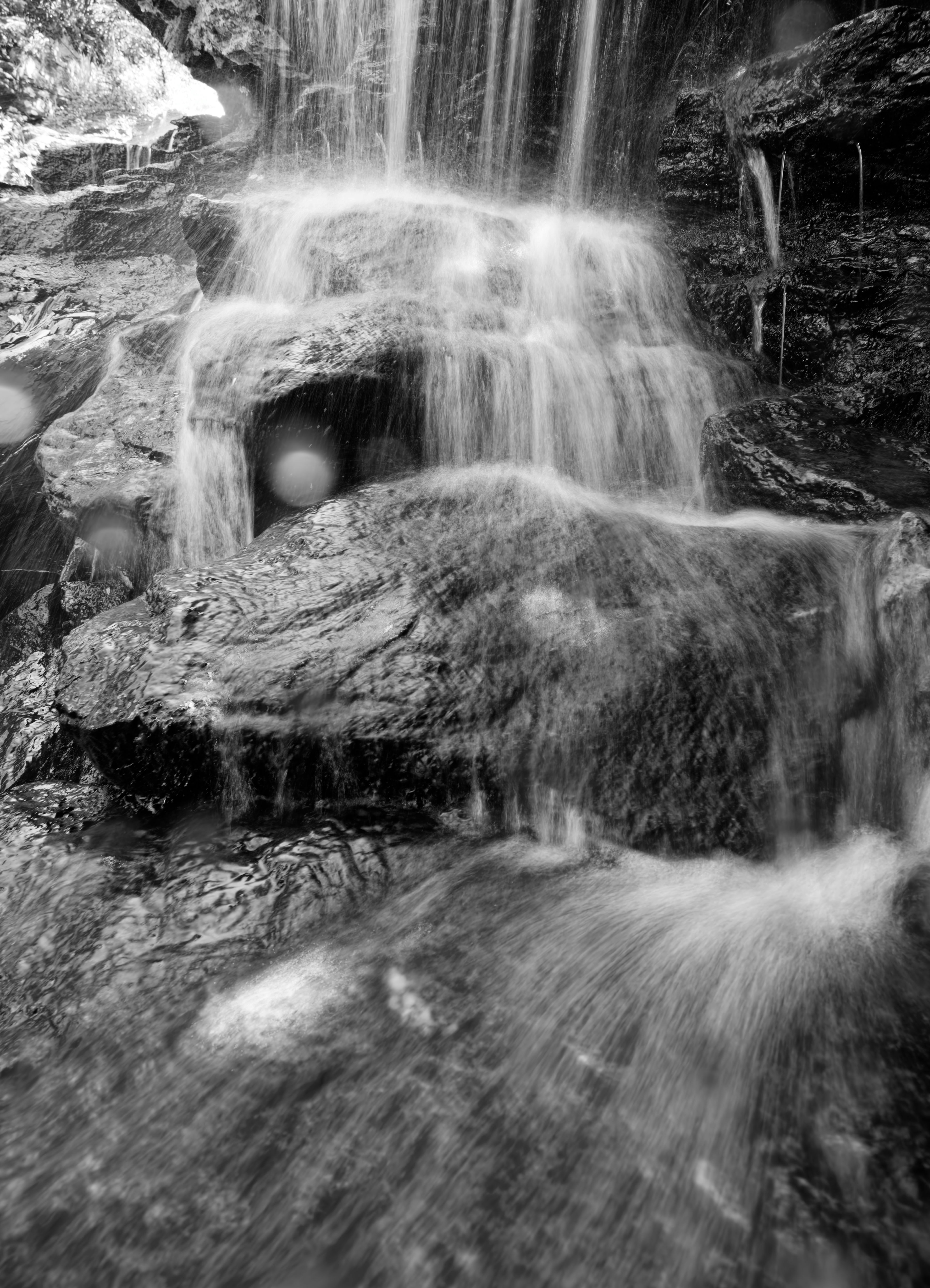 Cascata bianca e nera che scende su rocce ruvide.