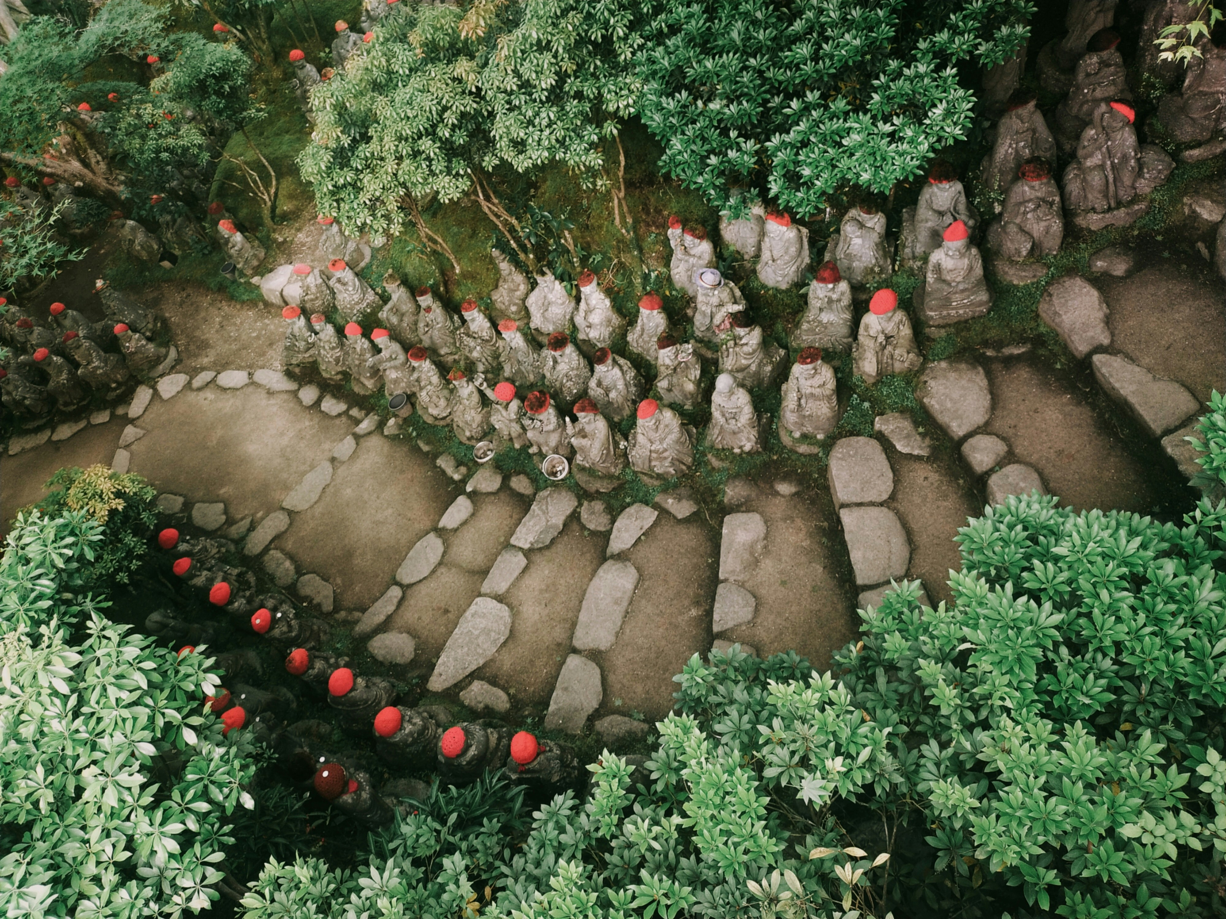 Stone statues with red hats along a winding garden path.