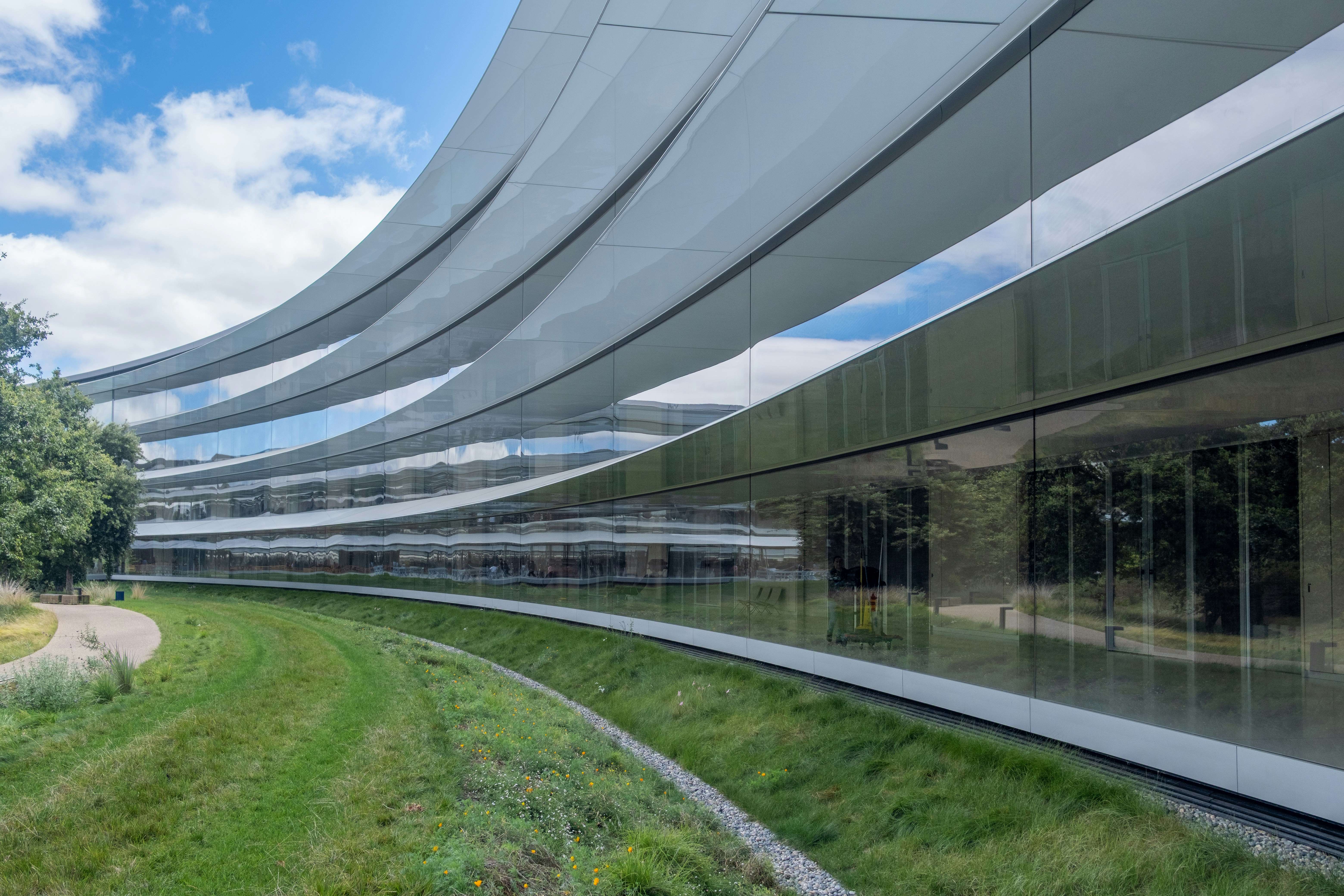 Sleek, curved building with glass facade and green landscape.