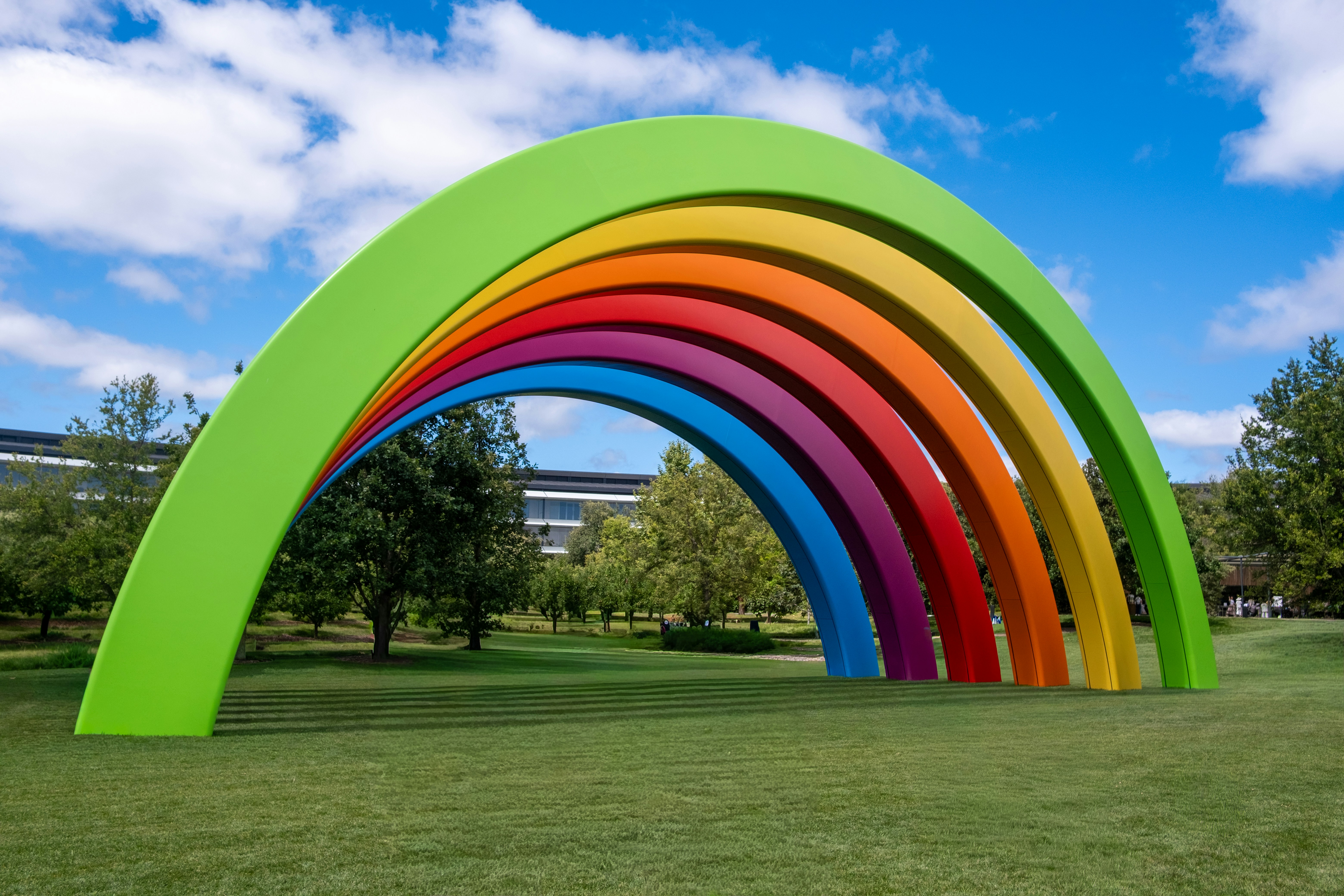 Vibrant rainbow arch sculpture on green grass under blue sky.