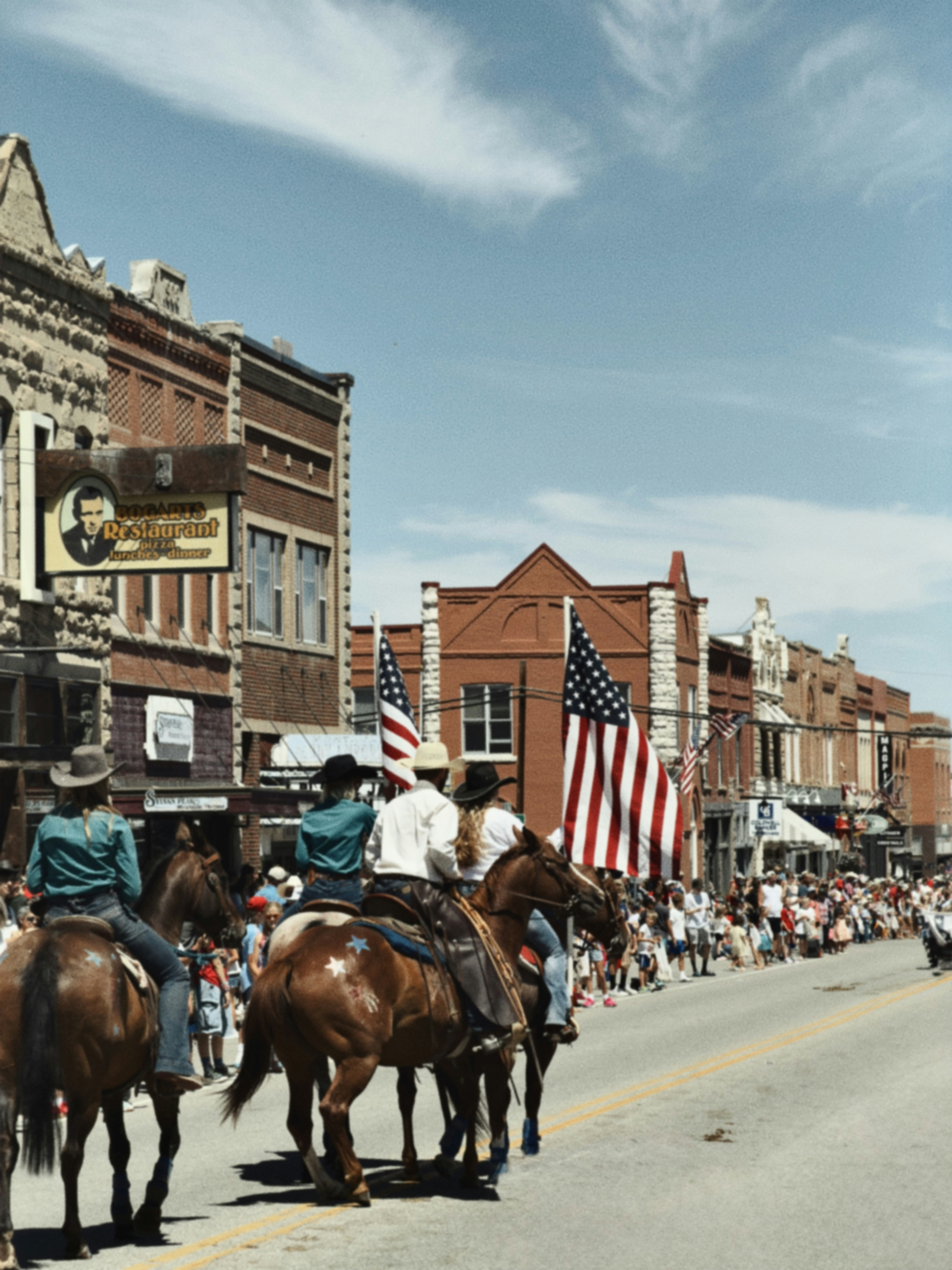 People on horseback parade down a street lined with flags.