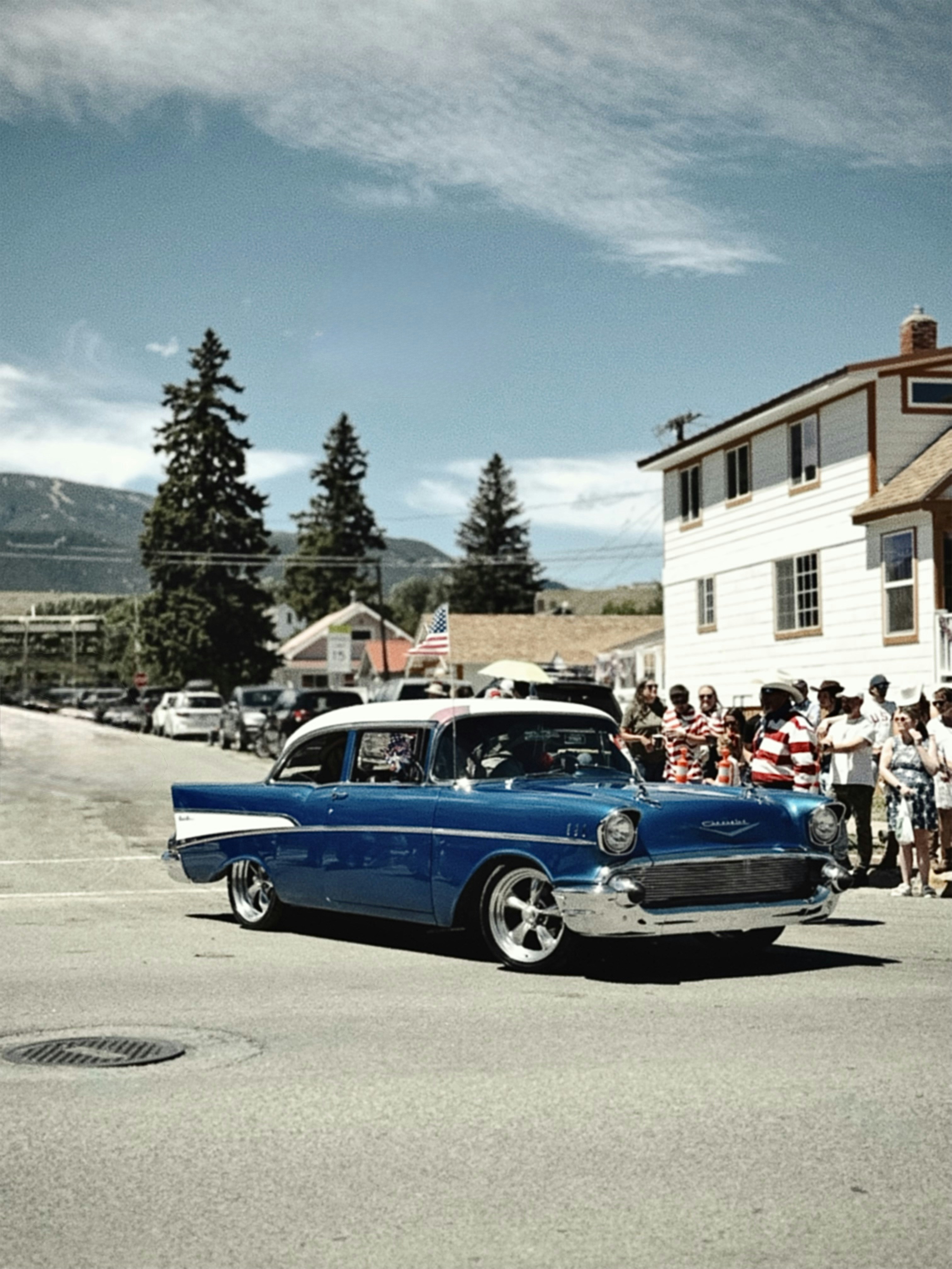 Vintage blue chevrolet driving past spectators on a sunny day.