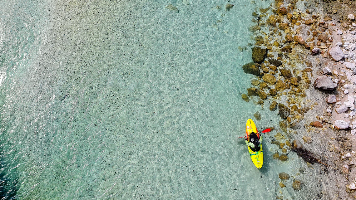 Kayaker exploring vivid turquoise river water beside a rocky shoreline