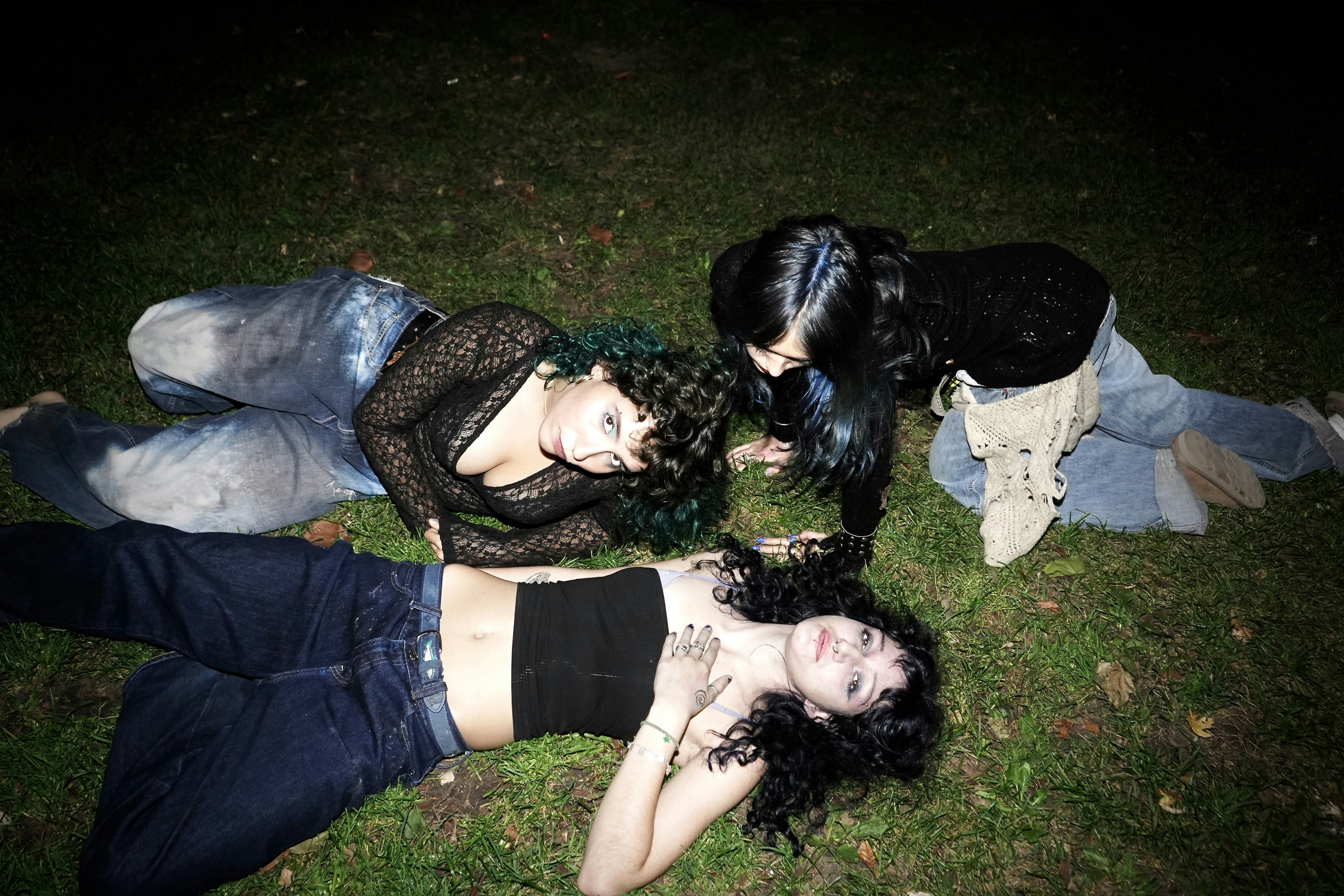 Três jovens mulheres deitadas na grama à noite