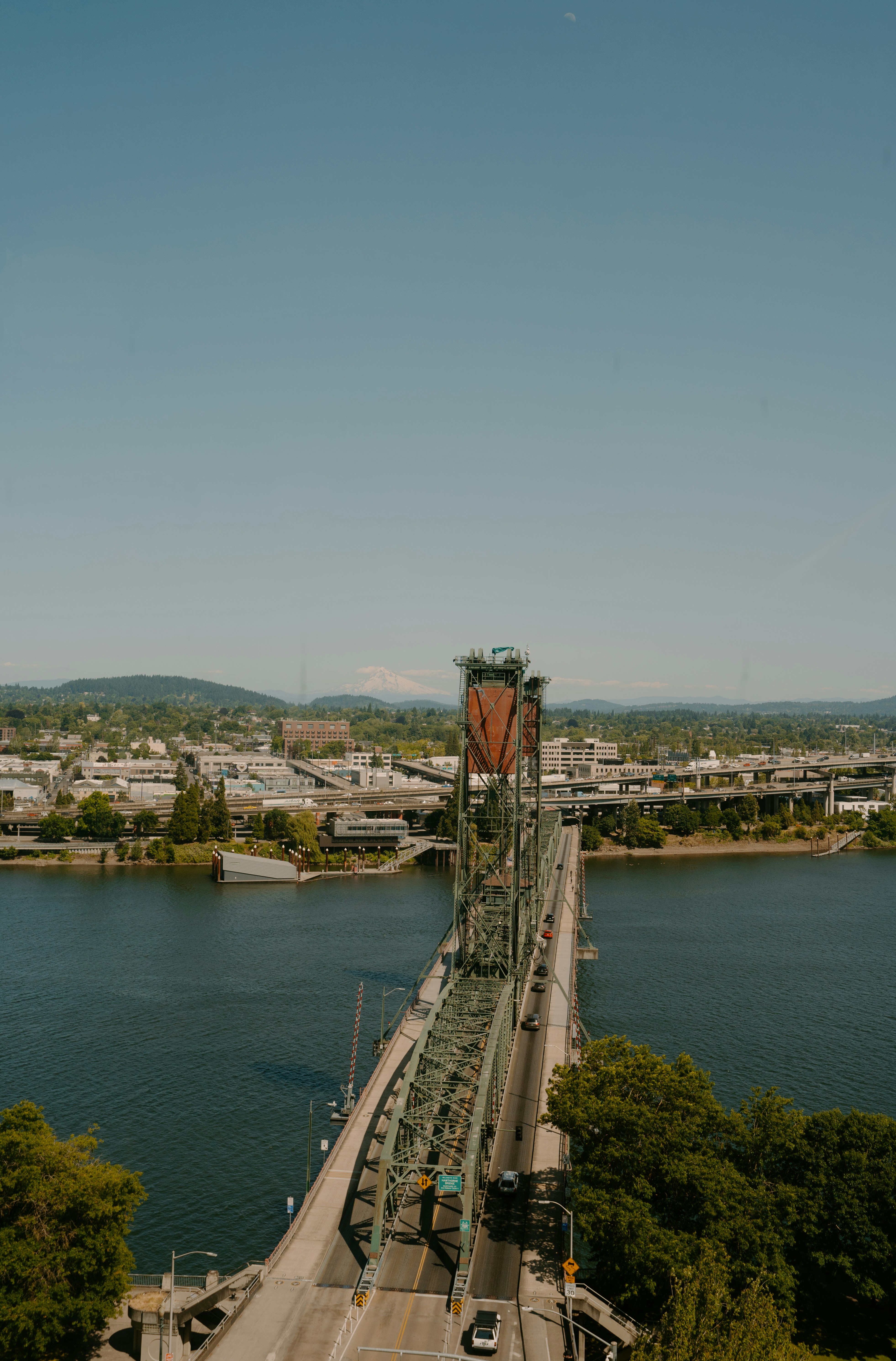 Green bridge over river with city skyline and clear sky