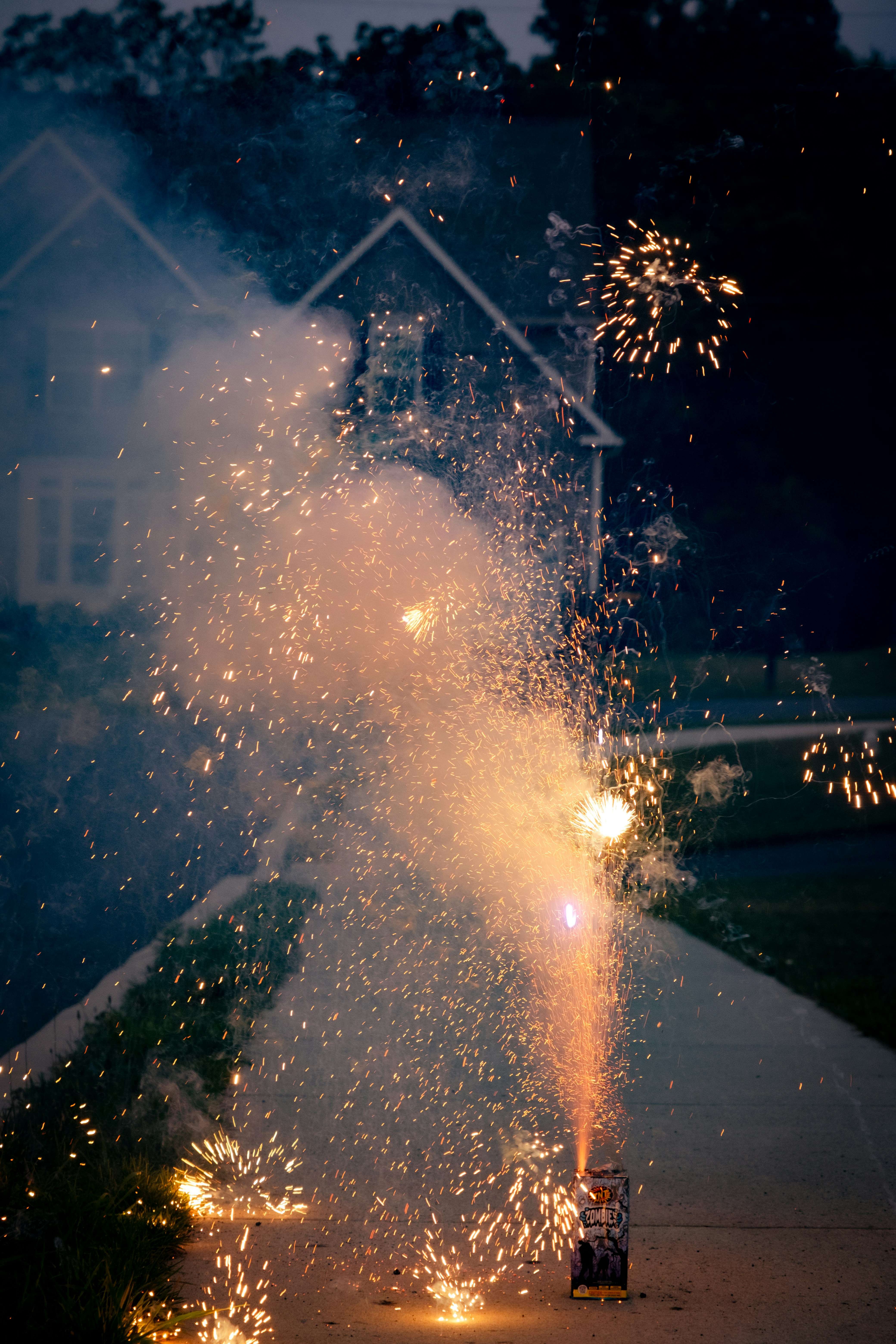 Fogos de artifício noturnos explodindo em uma entrada perto de uma casa.
