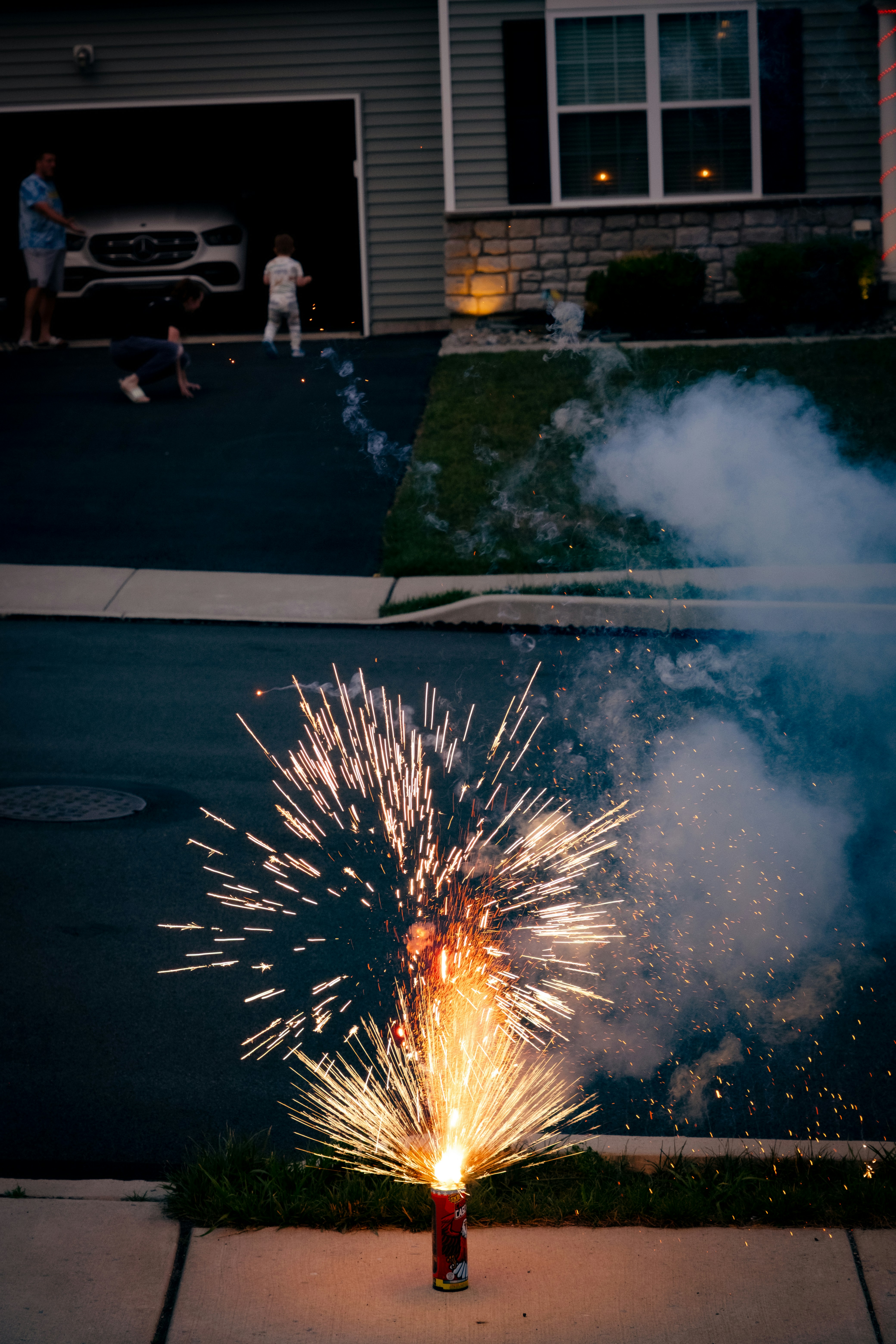 Fogos de artifício cintilantes explodem na calçada em frente a uma casa.