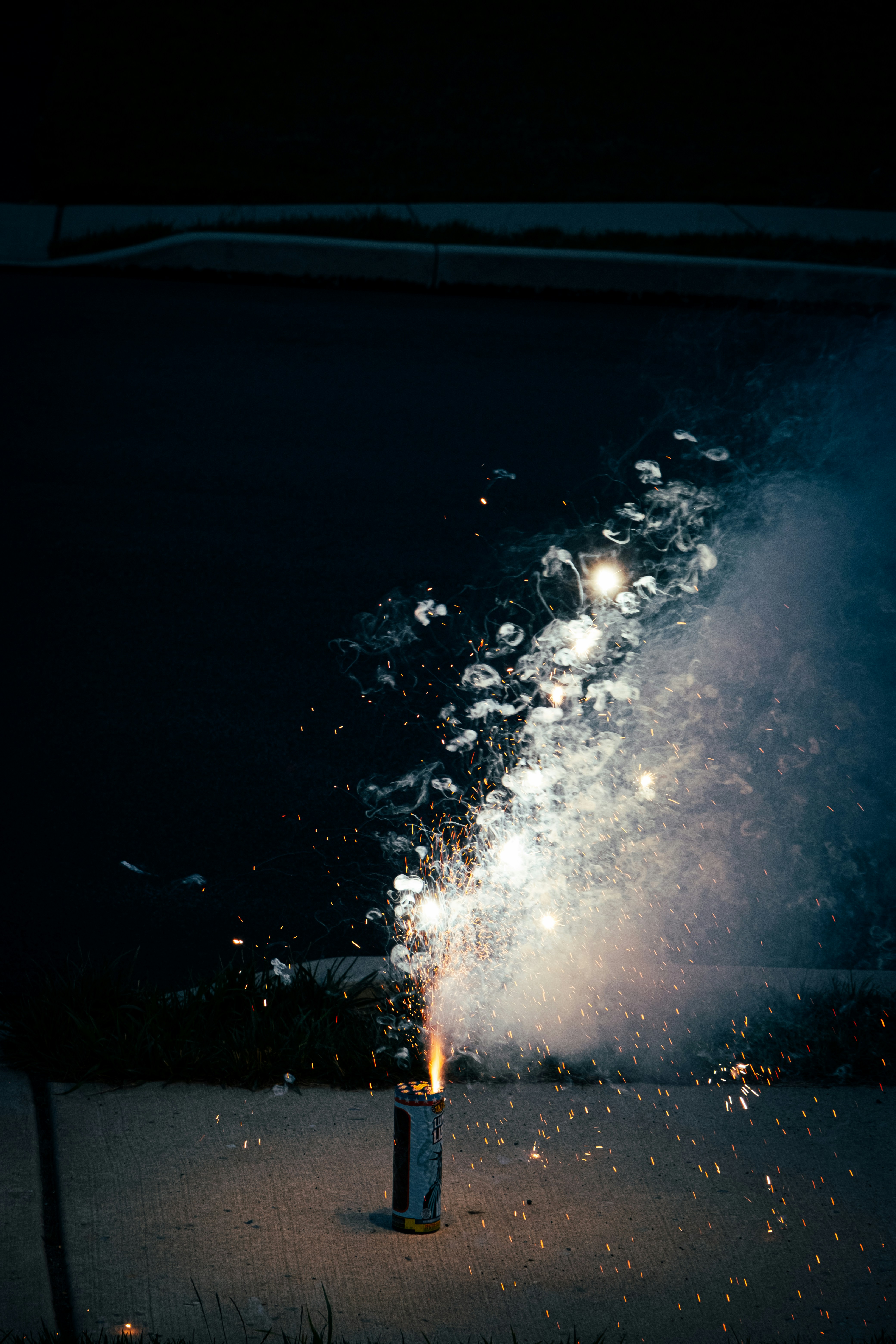 Um fogo de artifício se acende, emitindo faíscas brilhantes e fumaça à noite.