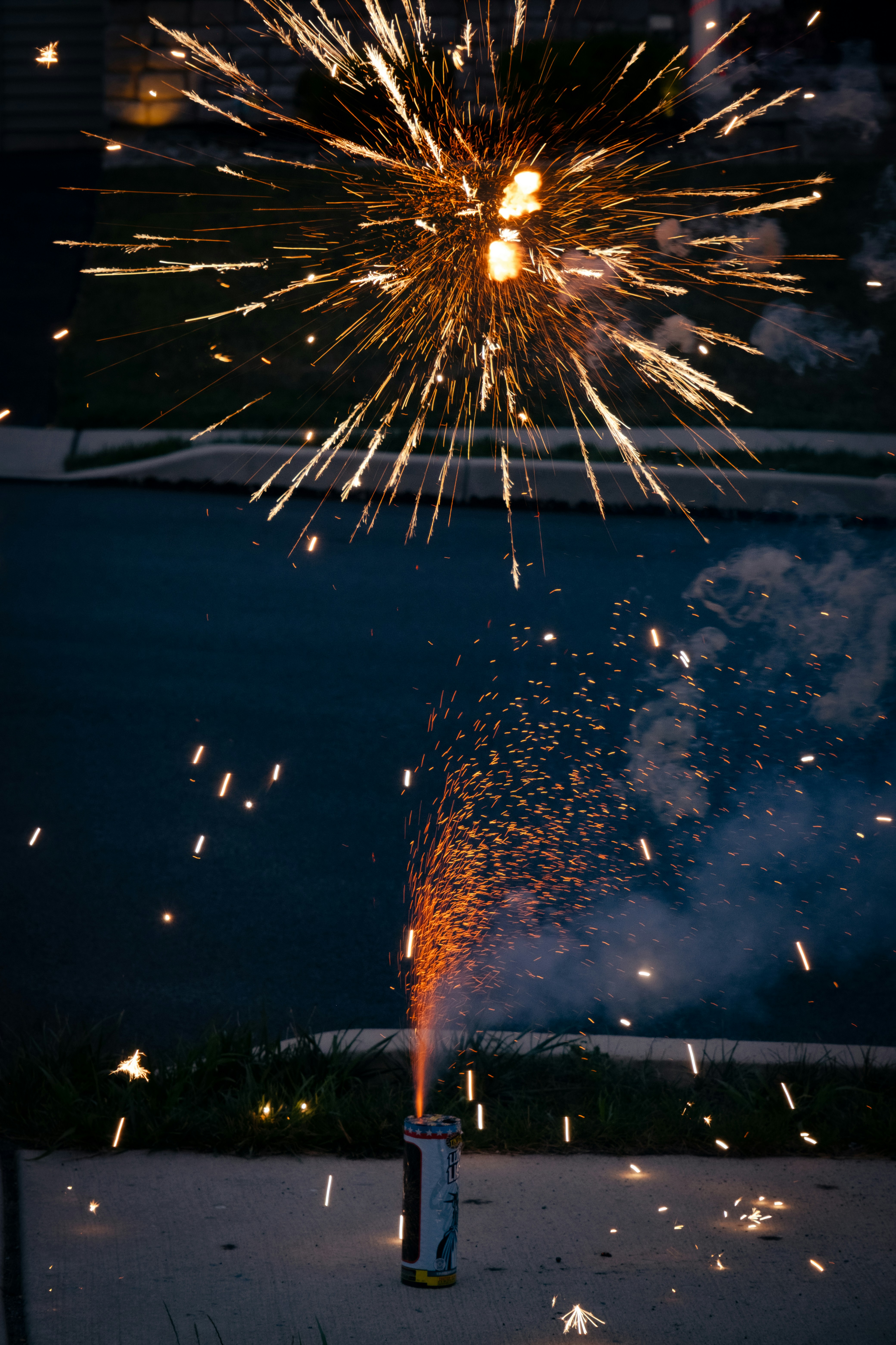 Fogos de artifício explodindo no céu noturno com uma fonte no chão.