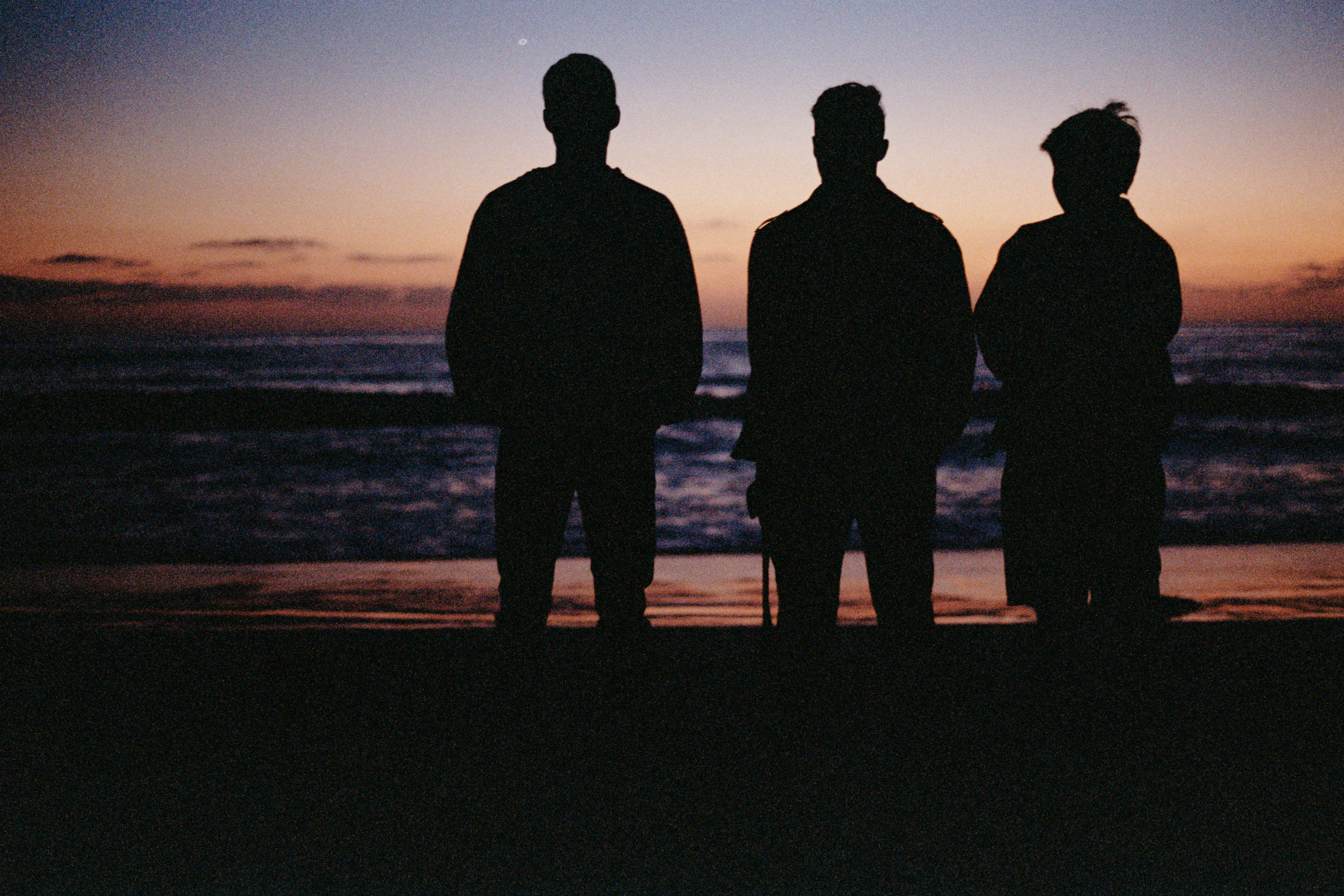 Three people silhouetted against a sunset over the ocean.