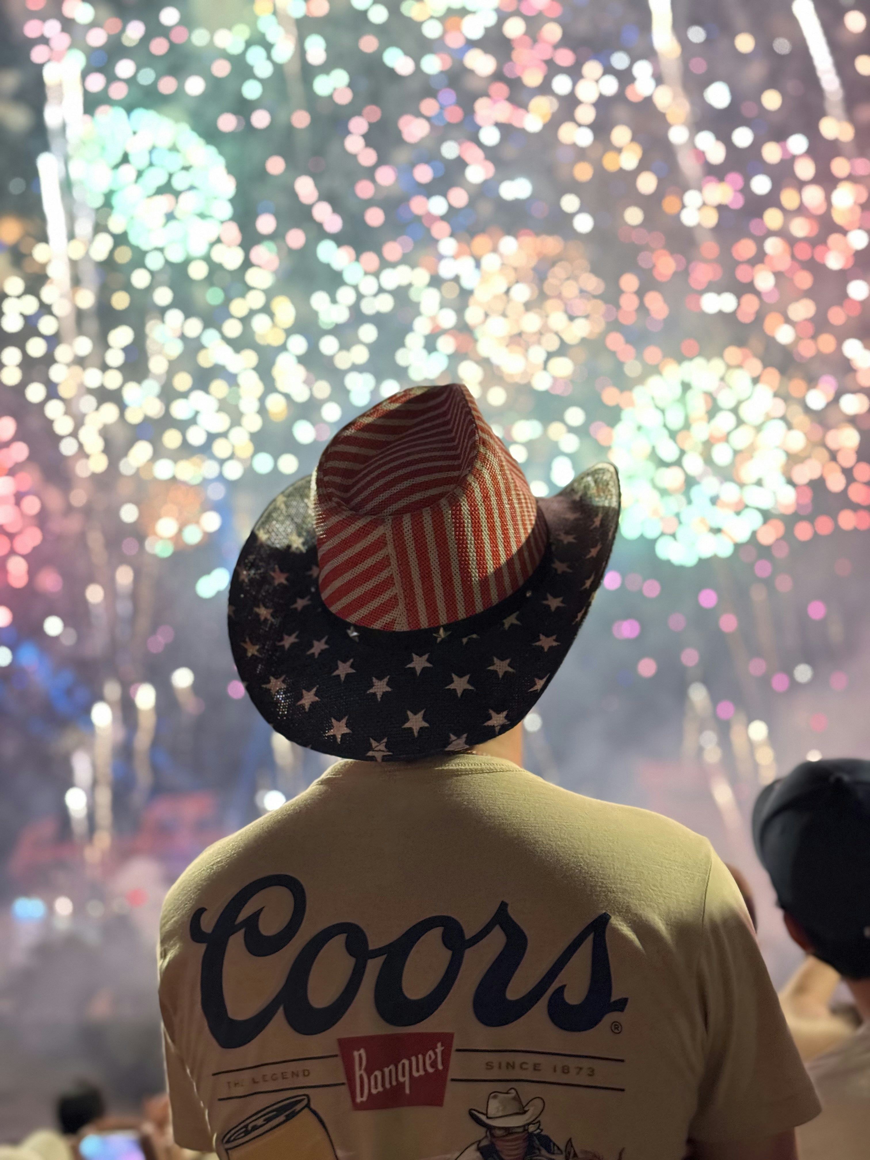 Personne au drapeau de cowboy américain regardant des feux d’artifice colorés.