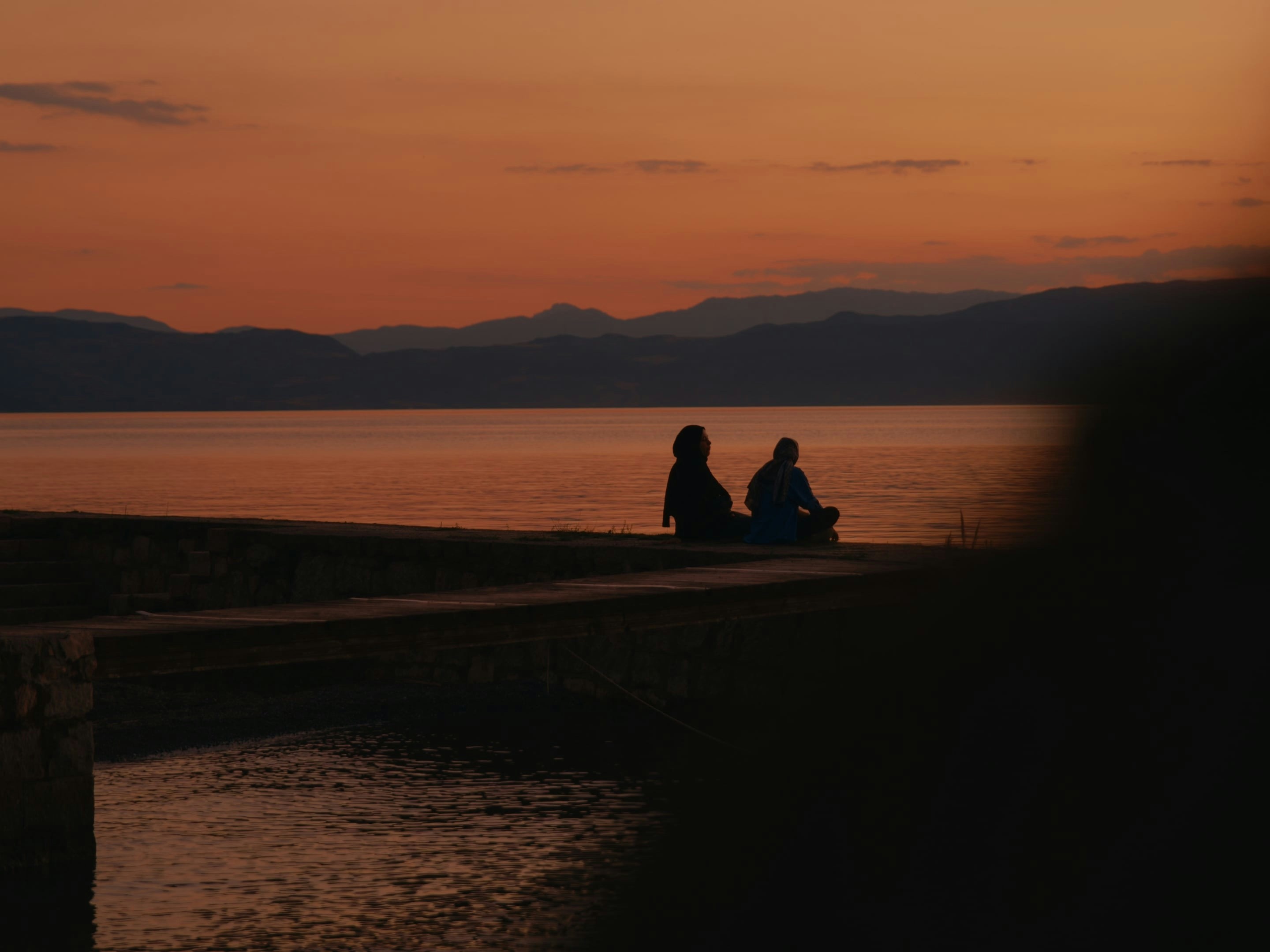 Zwei Menschen, die von einem wunderschönen Sonnenuntergang über einem See silhouettiert werden.