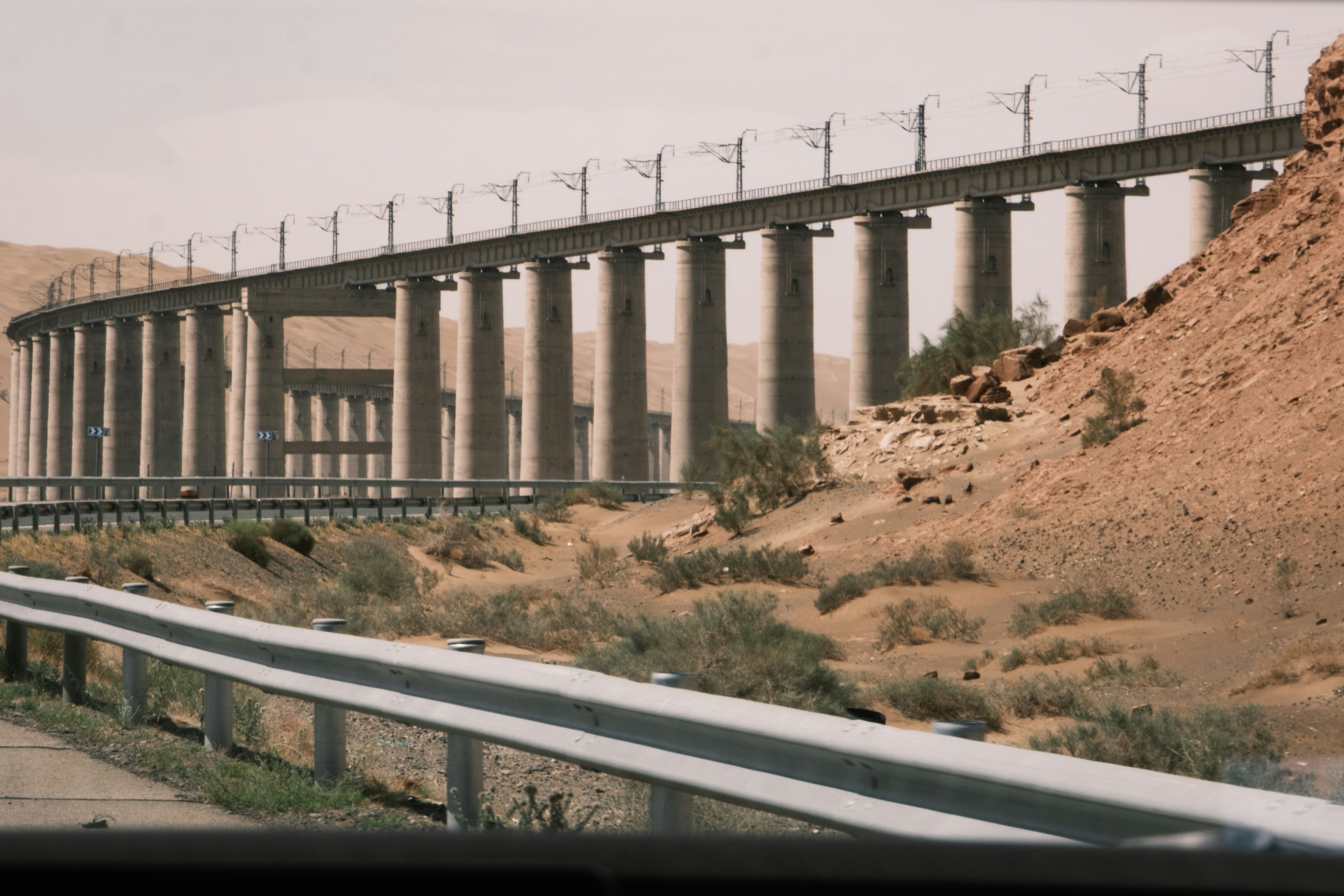 Curved concrete bridge in a desert with a road below.
