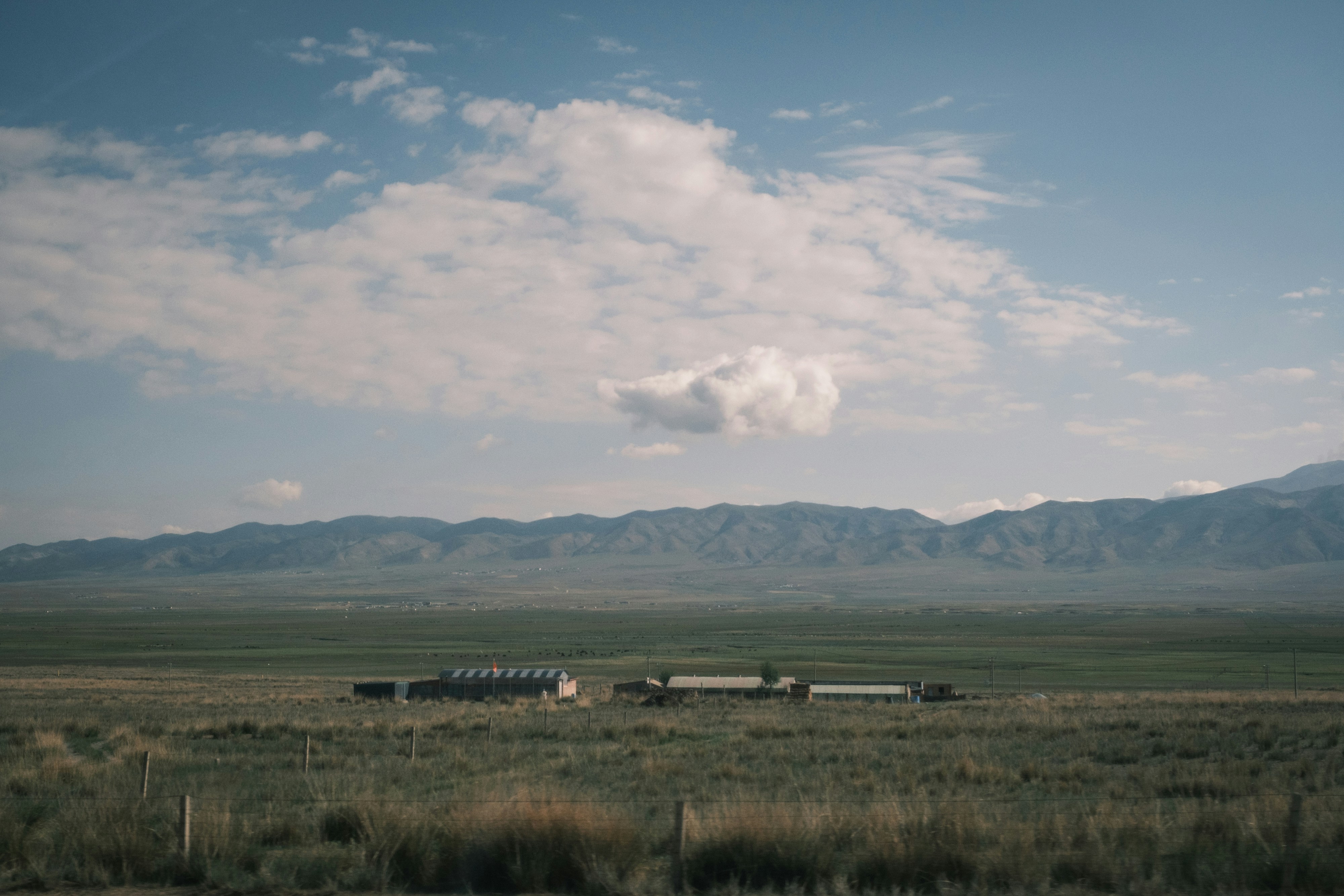 Farm buildings in a wide green valley with distant mountains.