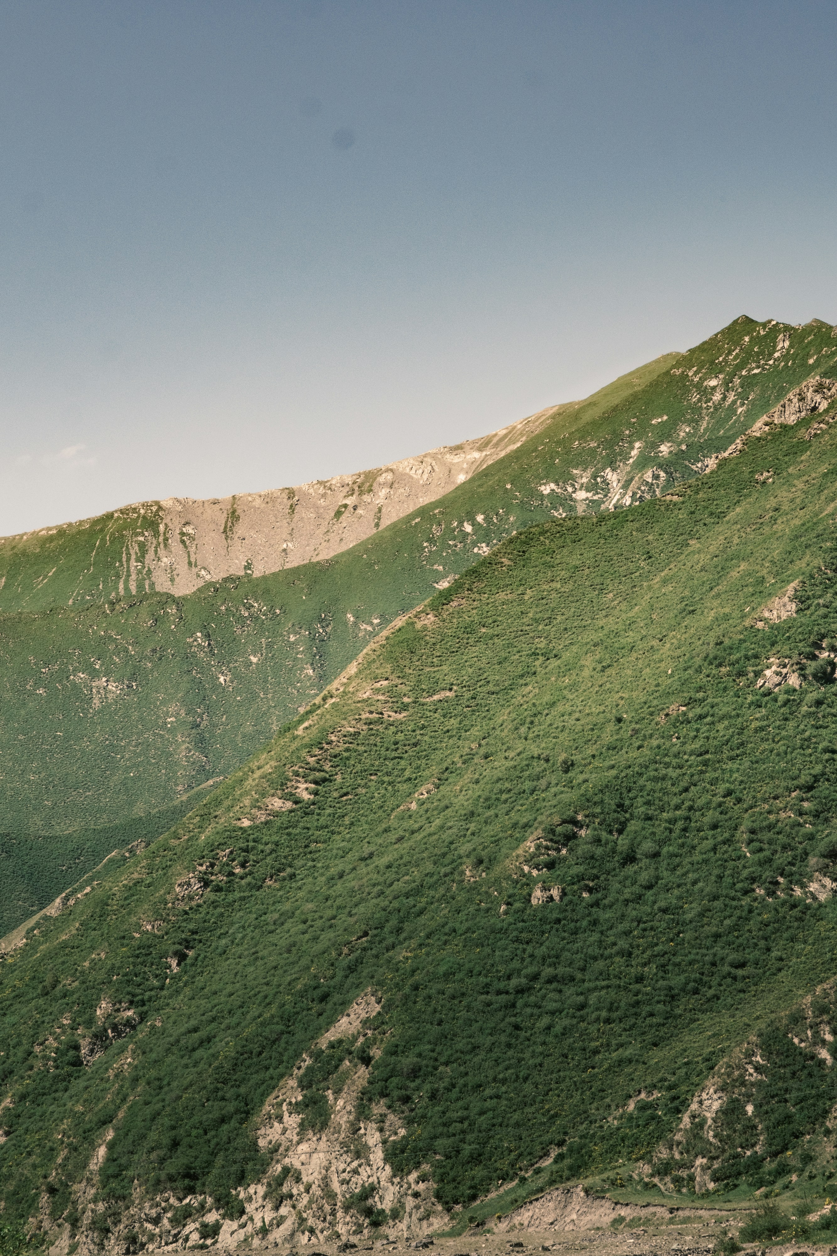 Green mountainside with rocky peaks under a clear sky.