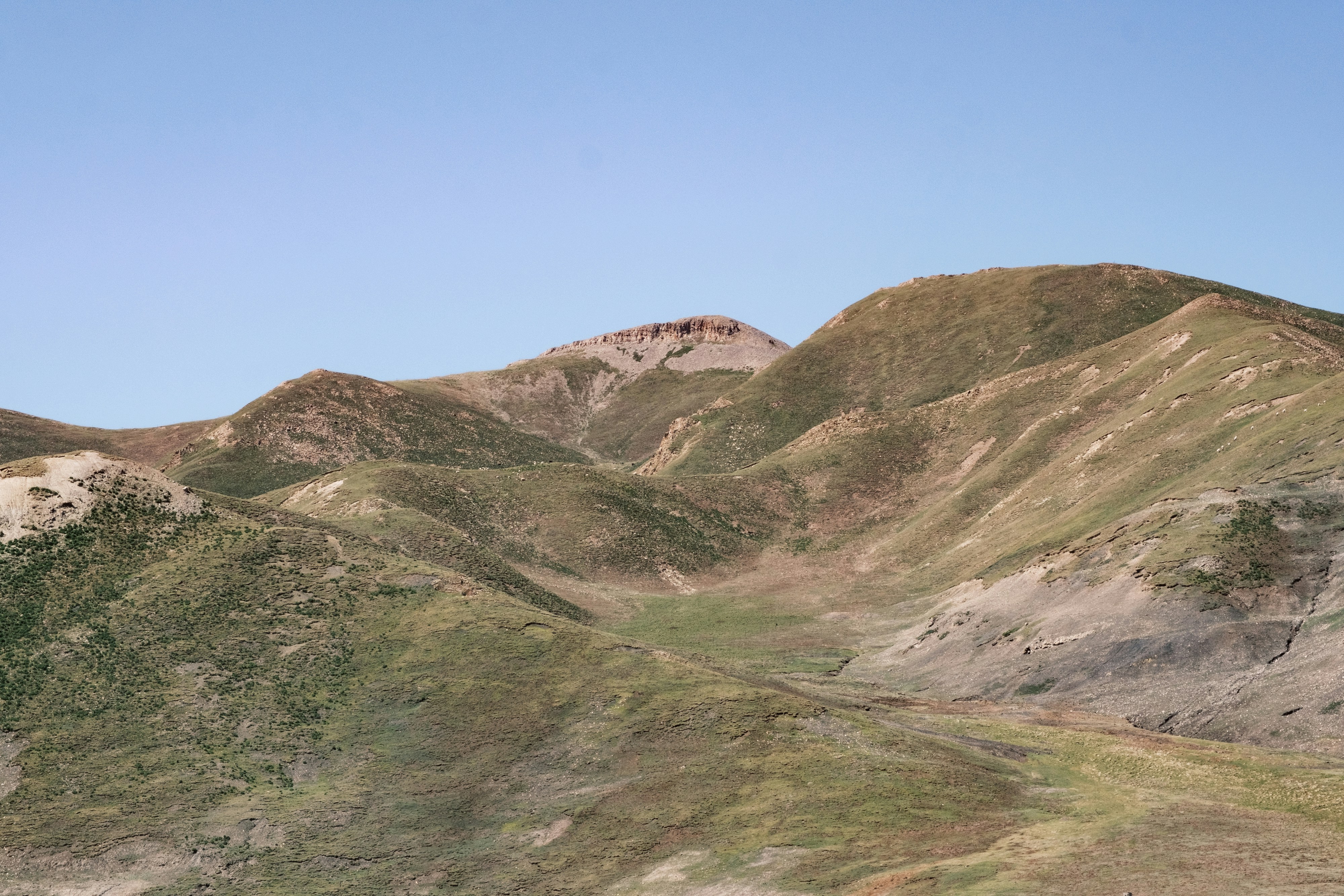 Rolling hills and mountains under a clear blue sky.