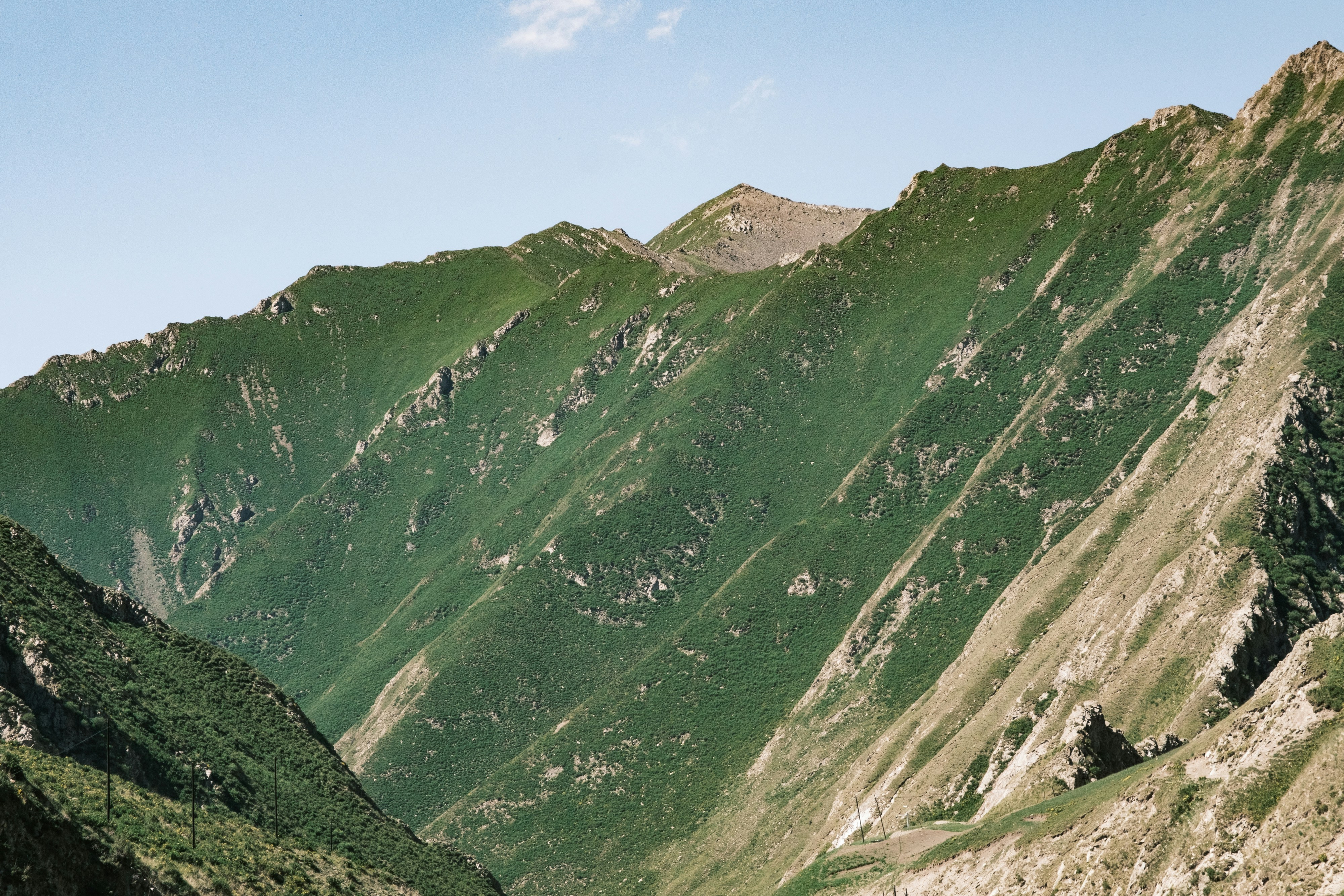 Steep, green mountains rise under a clear blue sky.
