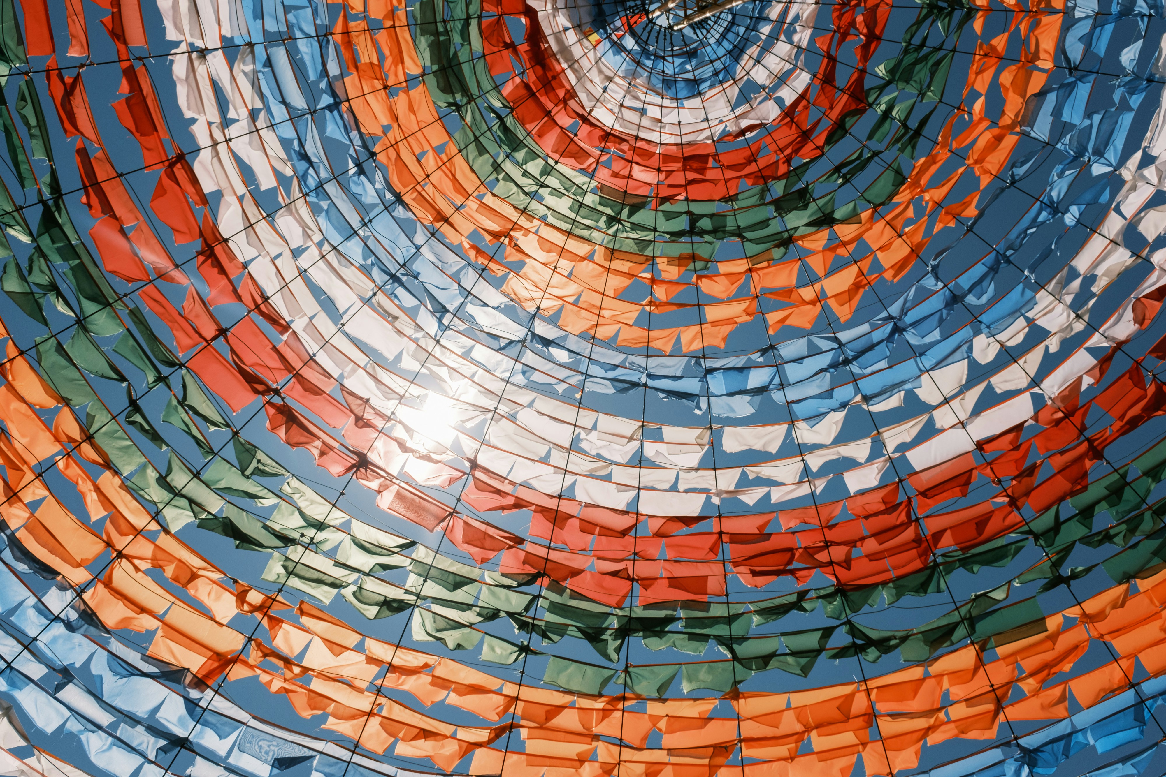 Colorful prayer flags arranged in concentric circles against blue sky.